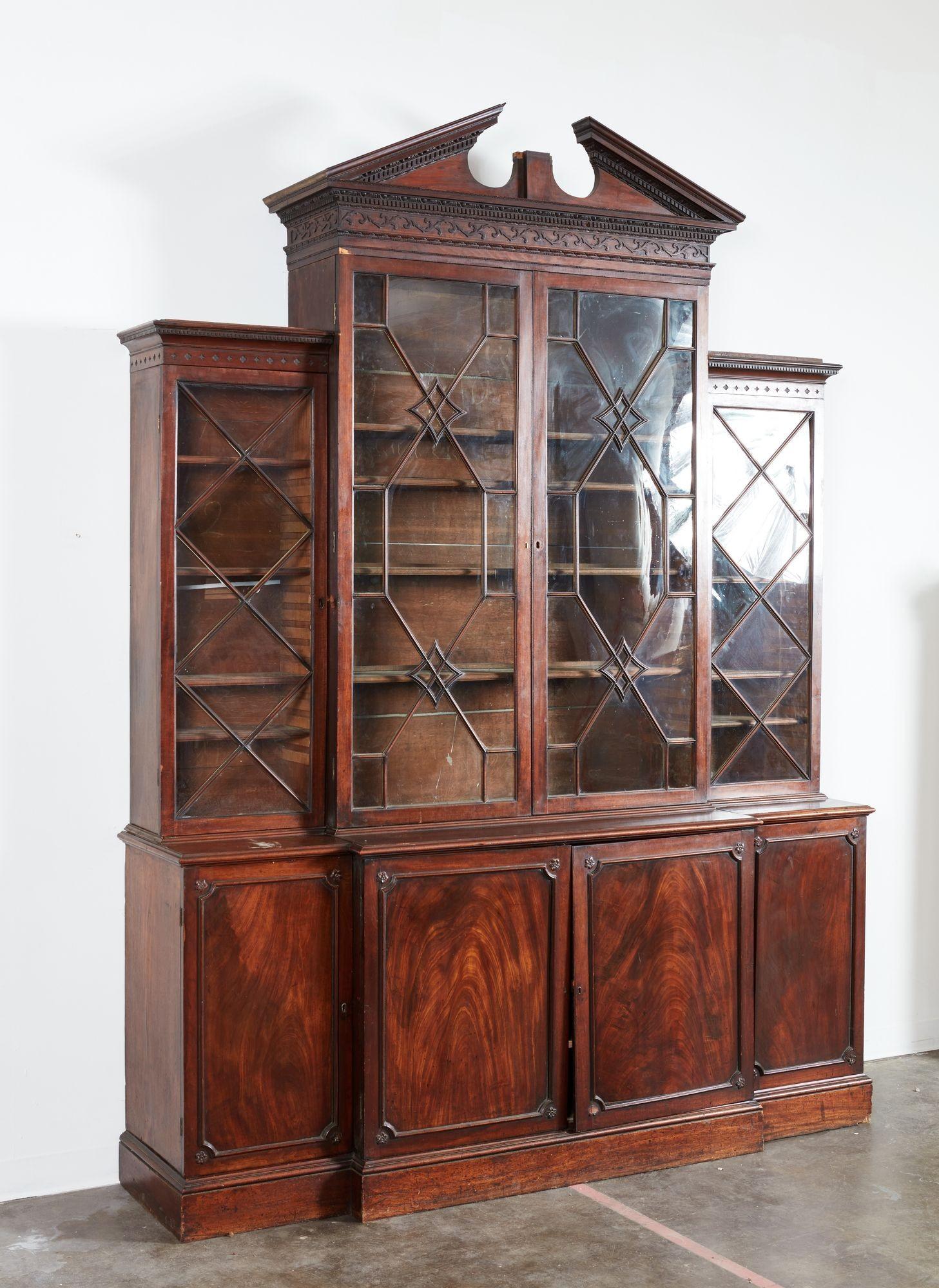 Pregevole libreria a due ante in mogano di George III alla maniera di Thomas Chippendale, con frontone architettonico a uovo e dardo con modanatura a dentello su fregio trattato in modo analogo e con volute a traforo cieche nell'alta sezione