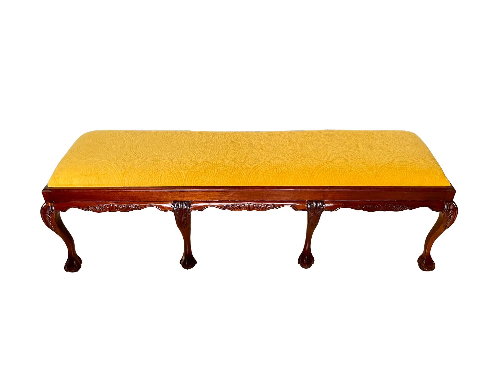 A late 20th century Chippendale style upholstered eight leg bench. Carved mahogany frame featuring a scalloped edge apron and cabriole legs with ball & claw feet. Recovered in a mustard yellow medallion tufted velvet.

Dimensions: 68