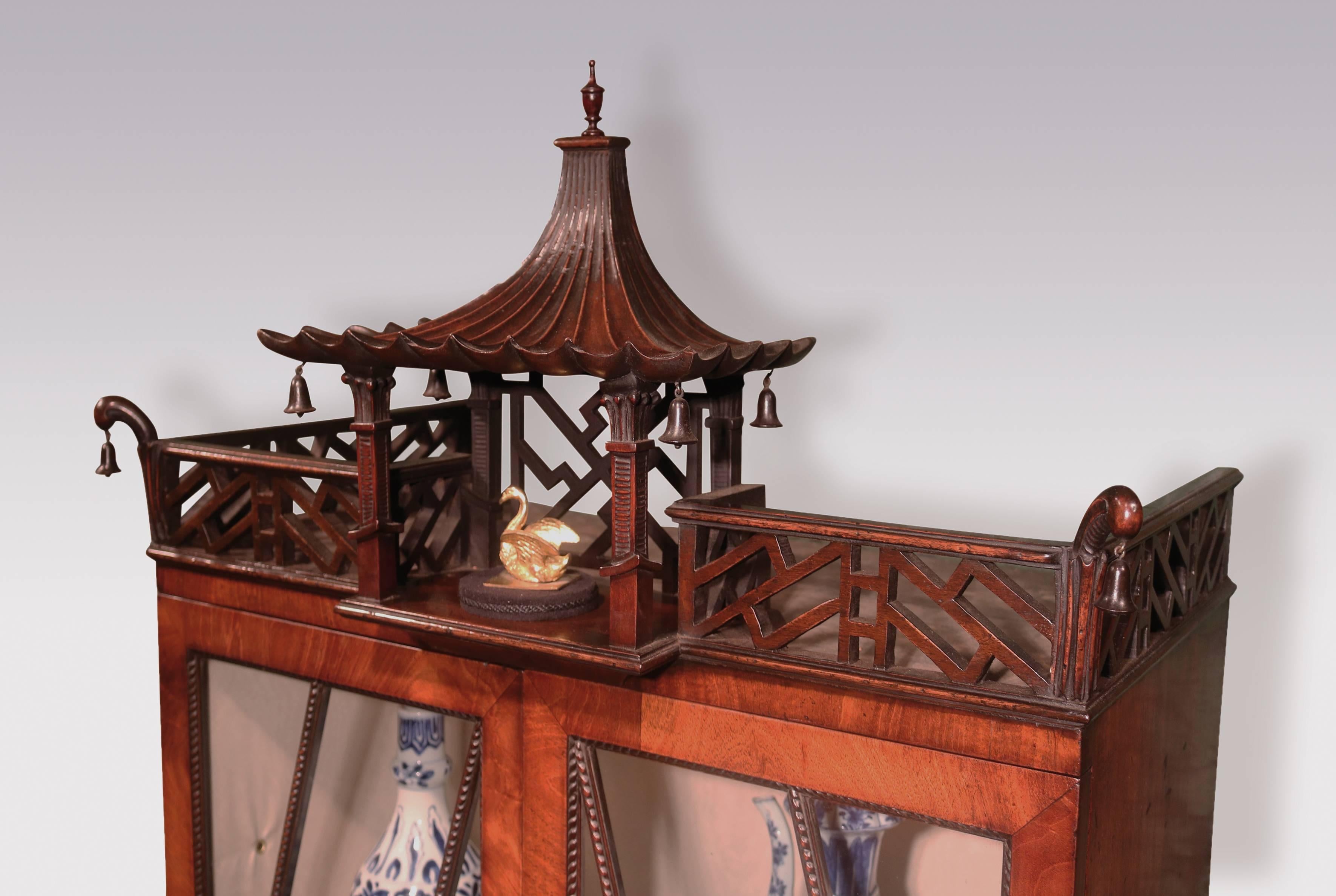 An unusual Chippendale design figured mahogany display bookcase of attractive small proportions, having pierced fretwork carved cornice with central gadrooned pagoda, above unusual angled gadrooned glazed doors, with carved gadrooned lower section