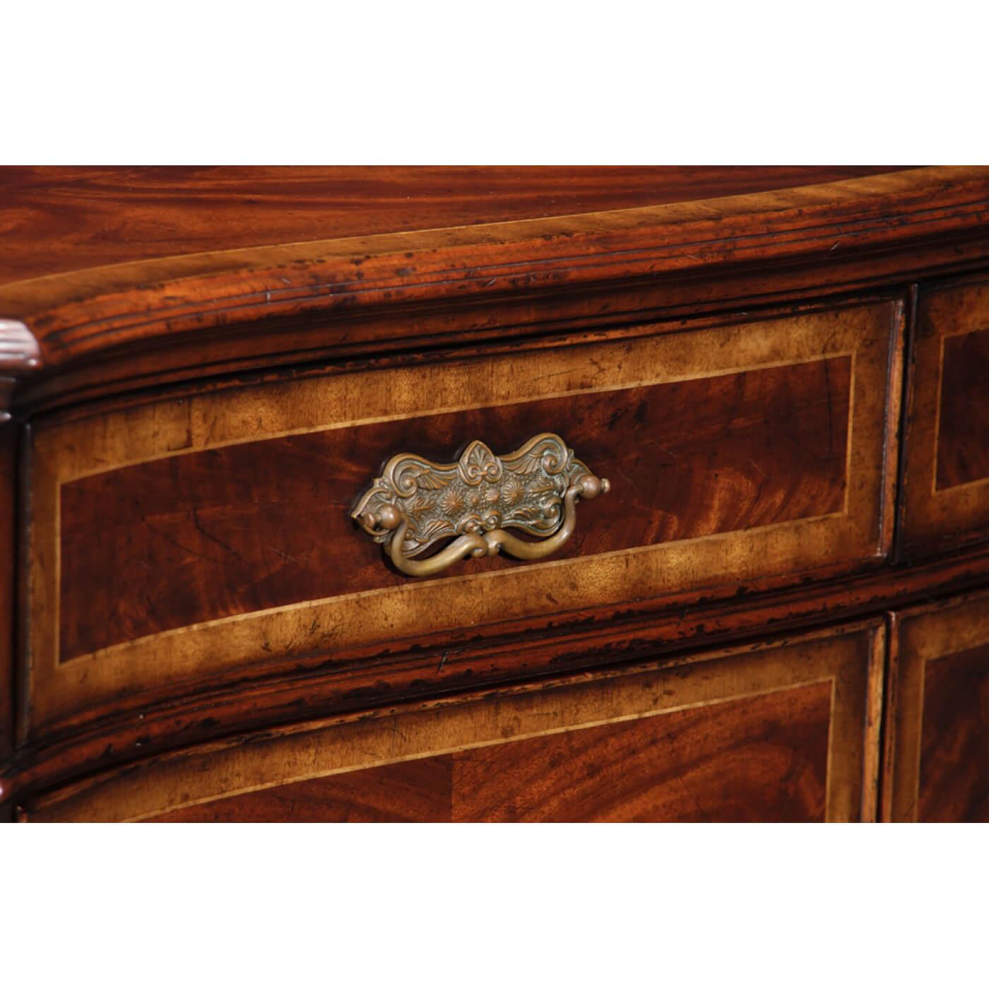 Crotch mahogany and crossbanded serpentine fronted side cabinet with canted corners of fluted columns with chip carving. Two shaped doors with drawers above, patinated brass handles and escutcheons, all raised on bracketed block feet.