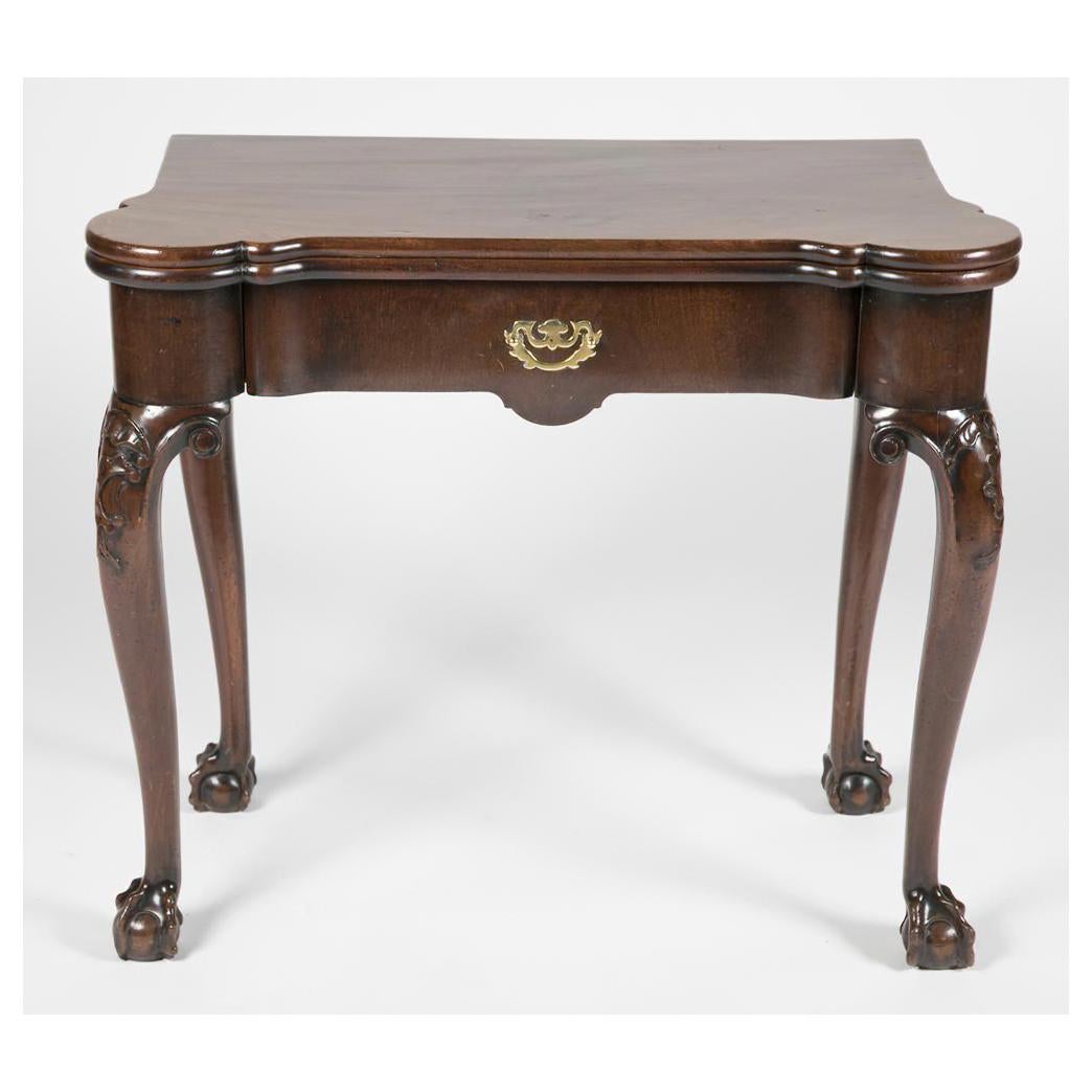 A George III Chippendale mahogany card table with turret corners and a shaped frieze, with a solid mahogany top on carved knee cabriole legs and boldly carved ball and claw feet.