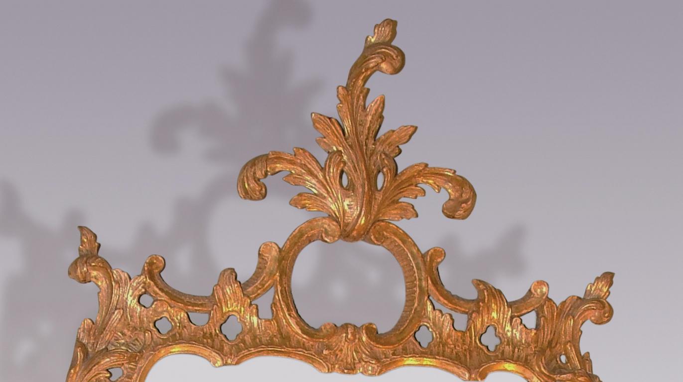 A mid-18th century Chippendale period carved giltwood looking glass, having scrolled cartouche above floral and bull rush C-scroll frame with replacement mirror plate.