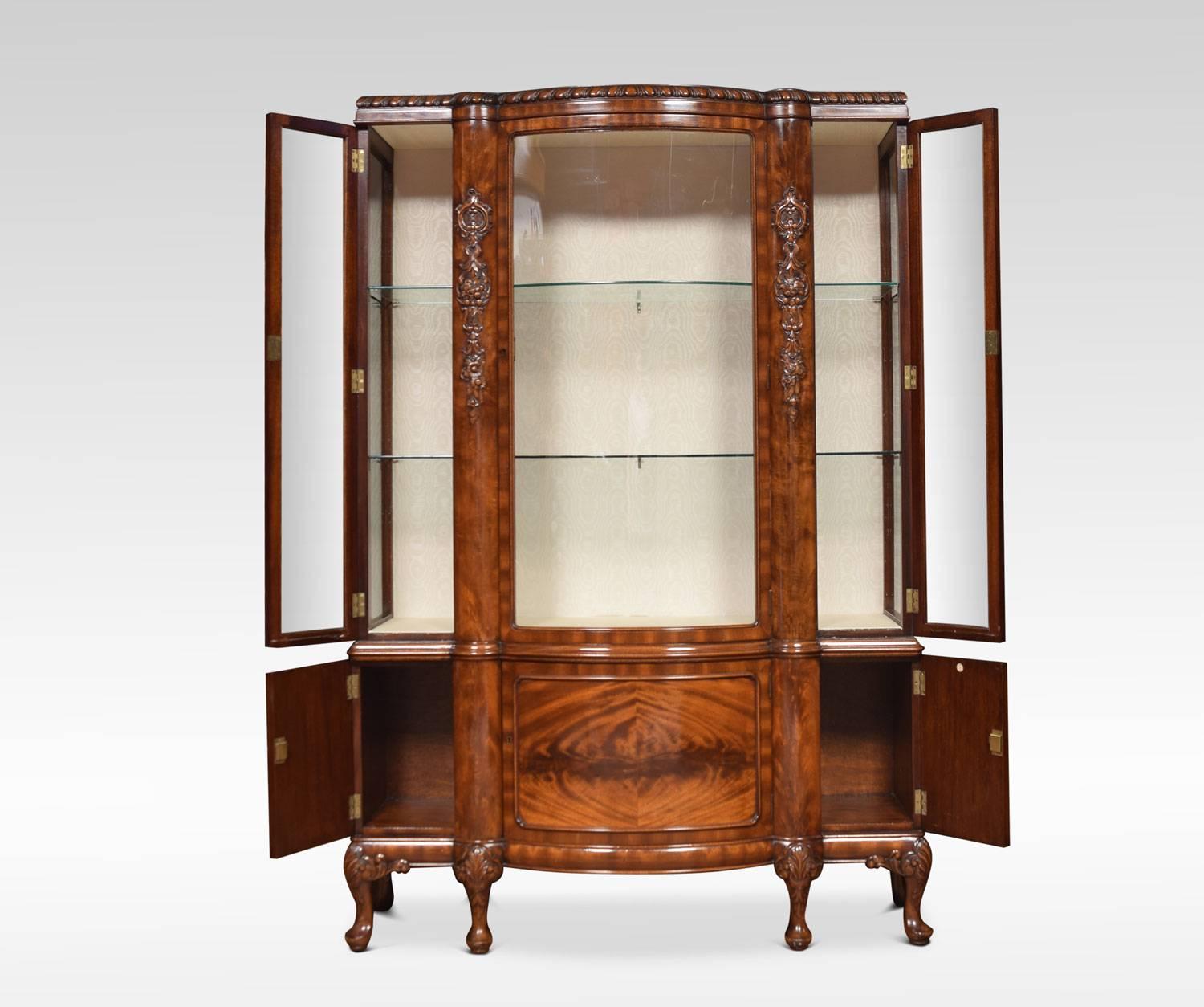 Chippendale revival mahogany bow fronted display cabinet the gradooned top above large central bow fronted door and shorter doors to either side. Flanked by carved scrolls and foliage. The cabinet fitted with two glazed shelves. The base section