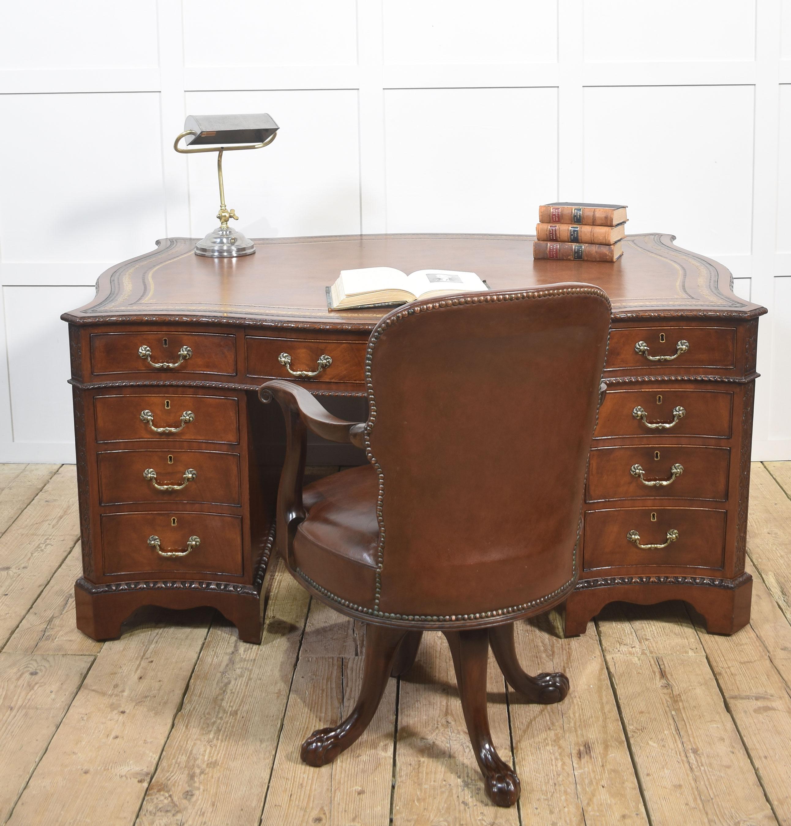 A finely crafted Chippendale Revival partner’s desk in rich mahogany, distinguished by its serpentine outline and elaborate carved ornamentation. The moulded edge encloses a gilt-tooled leather writing surface, the warm tones of which harmonise