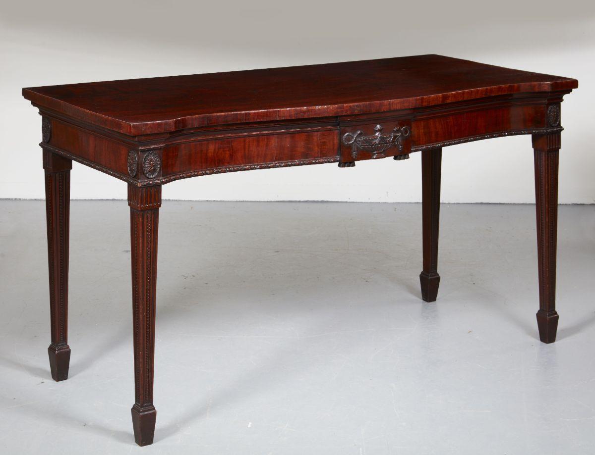 Very fine George III mahogany serving table attributed to Thomas Chippendale, the well figured serpentine top with deep under molding, the apron with central tablet featuring a carved snake handled urn with guttae drops, the apron with carved patera