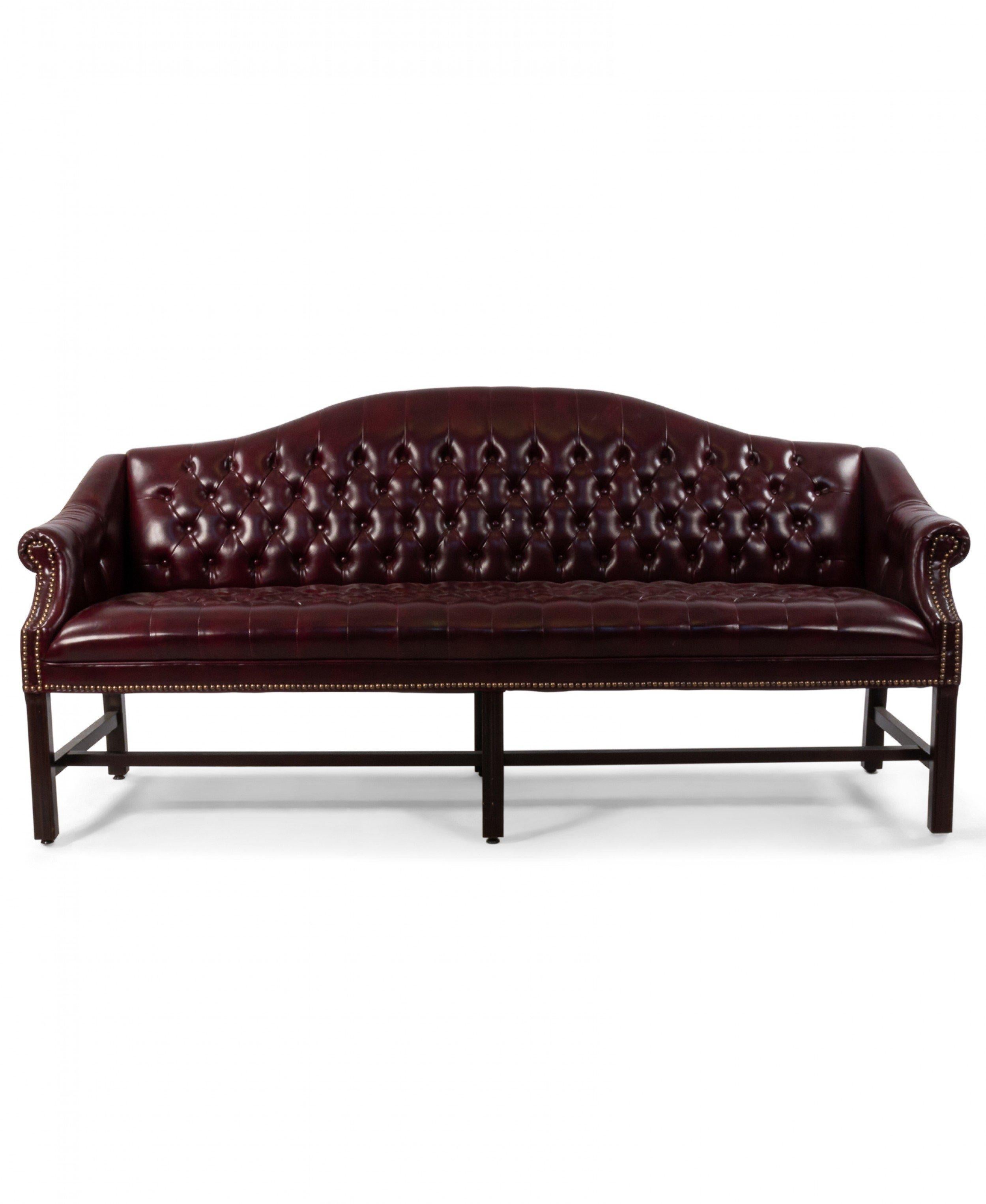 English Georgian style (20th century) burgundy leather camel-back button tufted chesterfield sofa with brass rivet trim supported on straight reeded legs and cross bar stretcher.