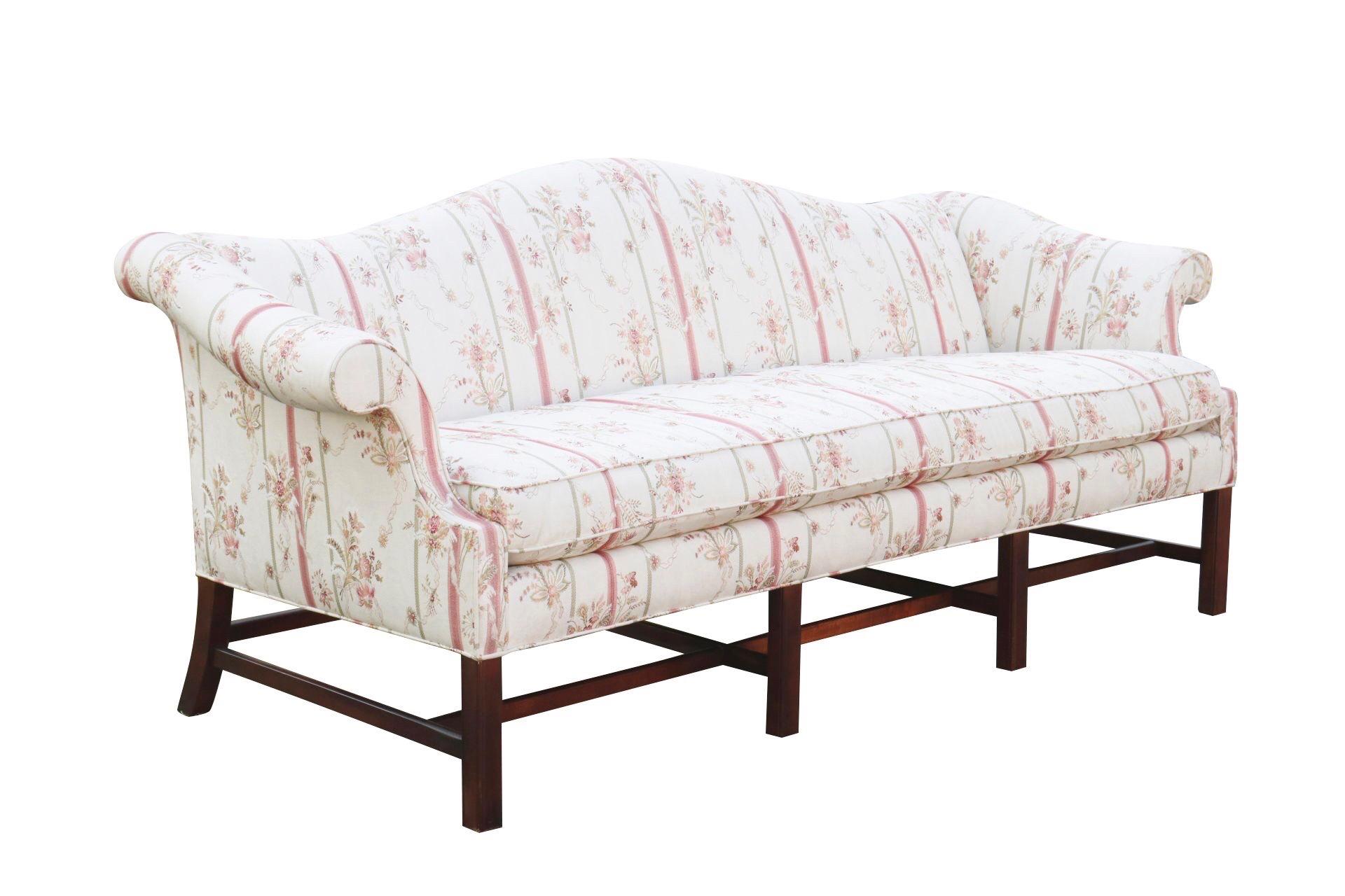 A Chippendale style camel back sofa made by Baker Furniture. The soft rolling camel back meets shapely outward rolled arms, upholstered in a floral ribbon striped fabric. A single bench cushion is down filled. Maker's label under the cushion reads