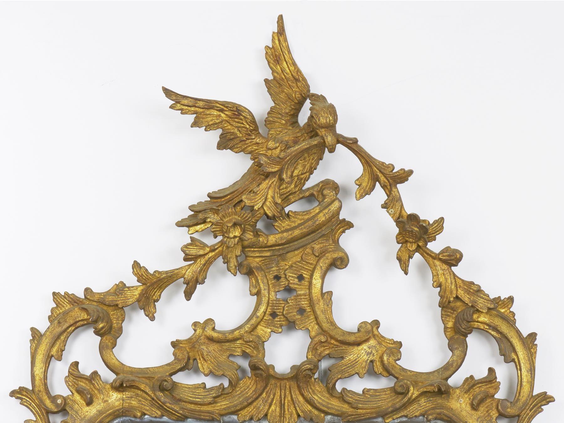 A most charming antique pier mirror, the oversized and beautifully hand carved phoenix cartouche is notable. Raised over a rocaille structure of opposing C-scrolls, the Phoenix holds a sprig of foliage in its beak, the vine proceeding to drape down