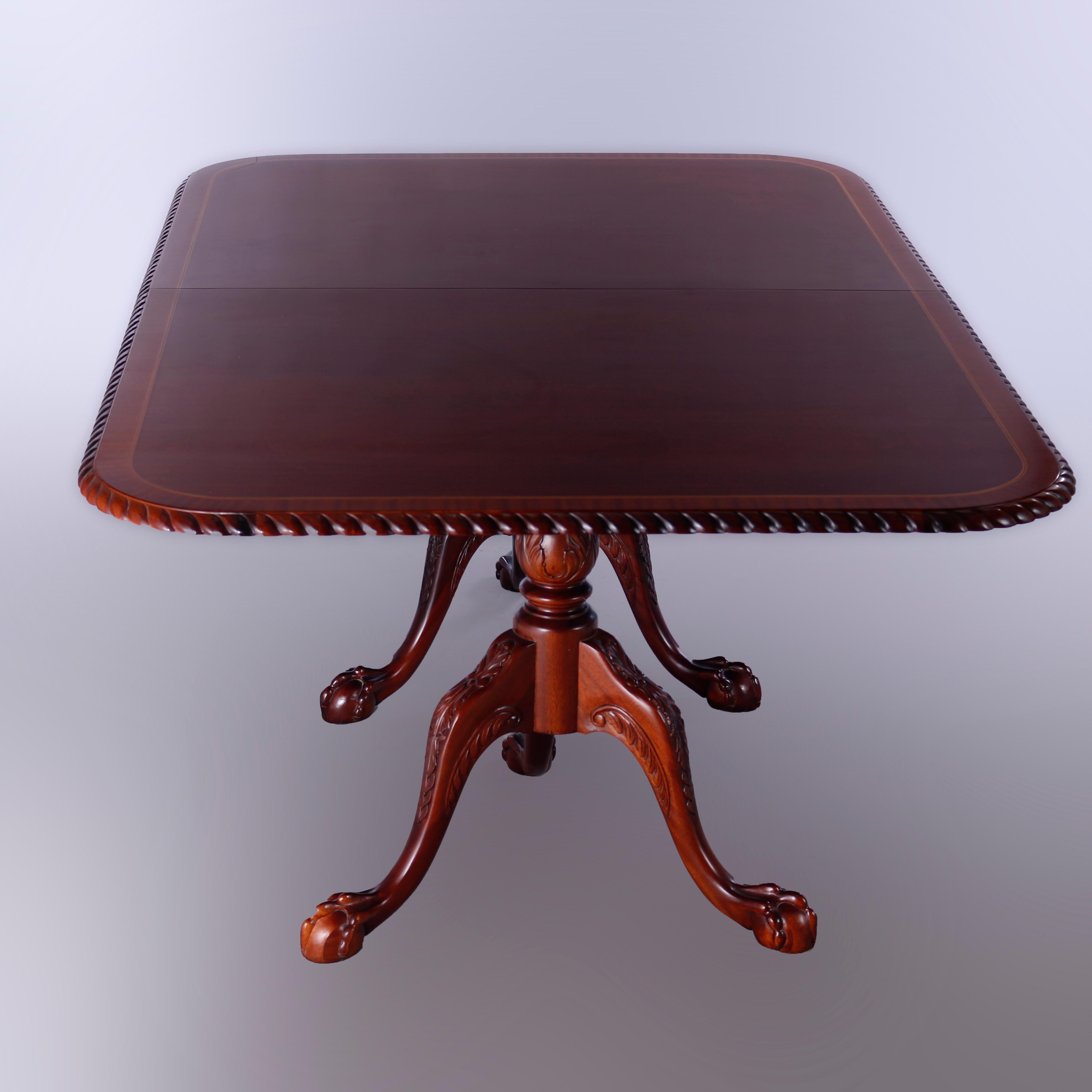 A Chippendale style dining table offers mahogany construction with cross banded top having rounded corners and carved gadrooned edge bordering, raised on double pedestals with cabriole legs terminating in claw and ball feet, extends to accept single