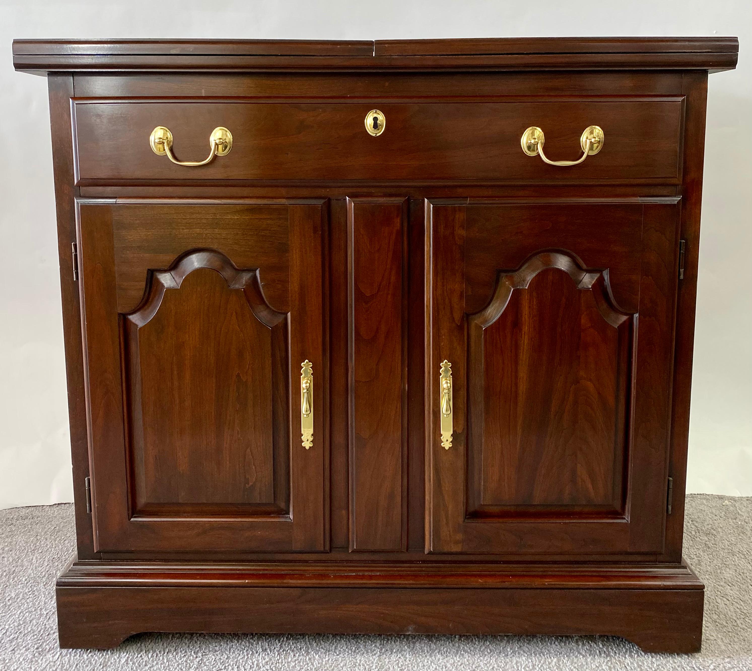 A quality solid Cherry wood cabinet or serving bar by Harden furniture. The cabinet features a single drawer over door cabinet. Each cabinet has one shelf. The top of the cabinet painted in black unfolds from both sides to offer more space for