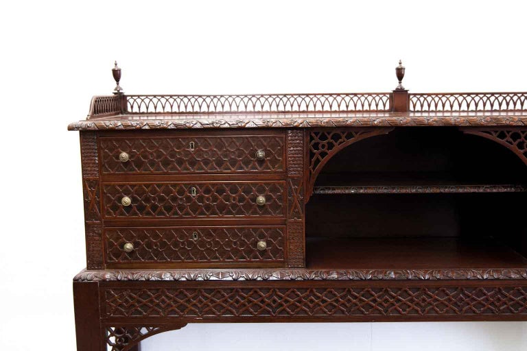 Chippendale style console table, the top with open fretwork gallery, corner and center turned finials, carved top molding, open center below with recessed shelf and open fretwork corner brackets, the six drawers featuring blind fretwork. The base