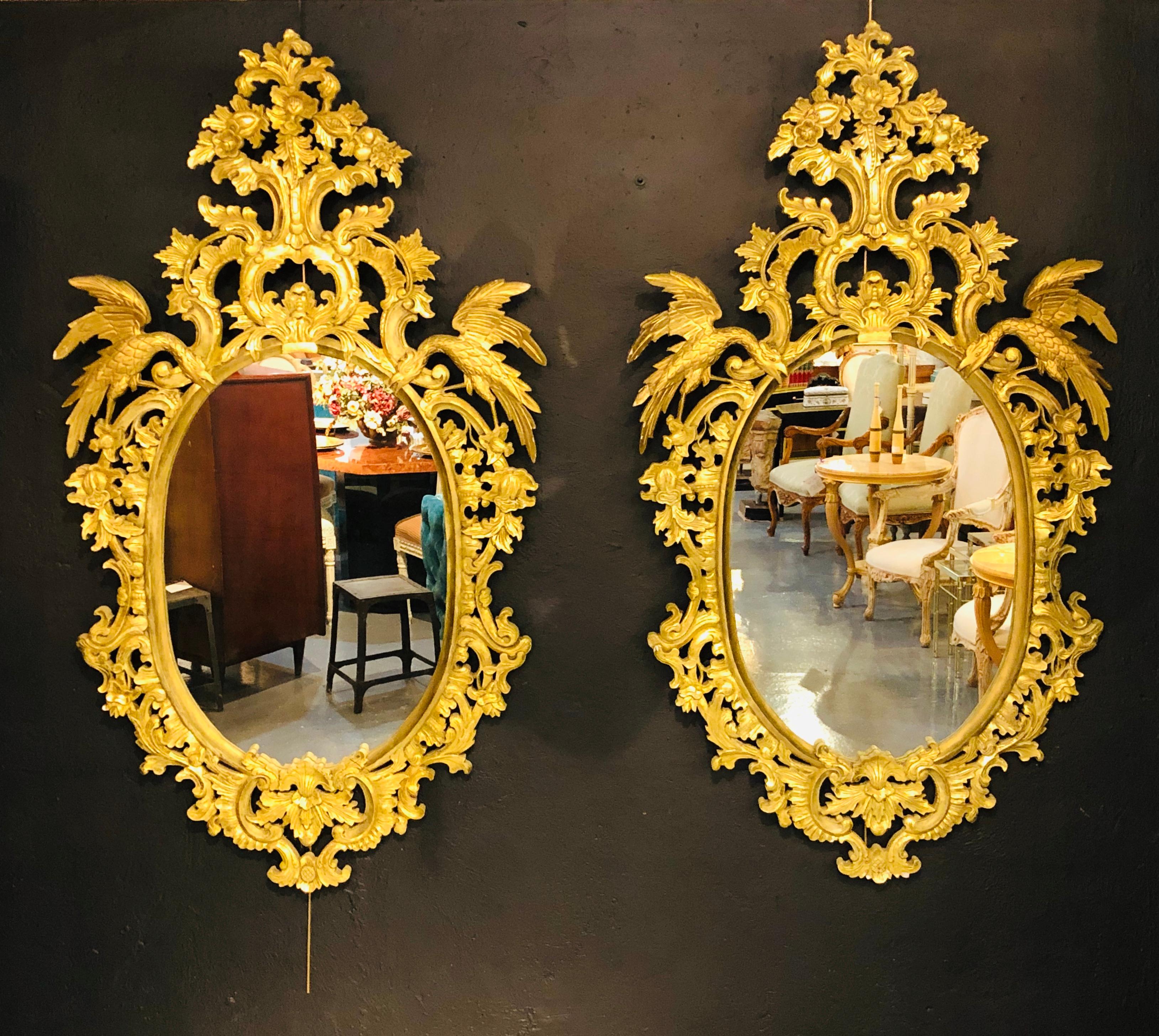 Pair of Chippendale style elaborate giltwood wall or console mirrors. The pair oval in form with a clean center mirror flanked by a finely carved carved frame of roses, floral design and scroll having full bodied winged birds perched on each side of
