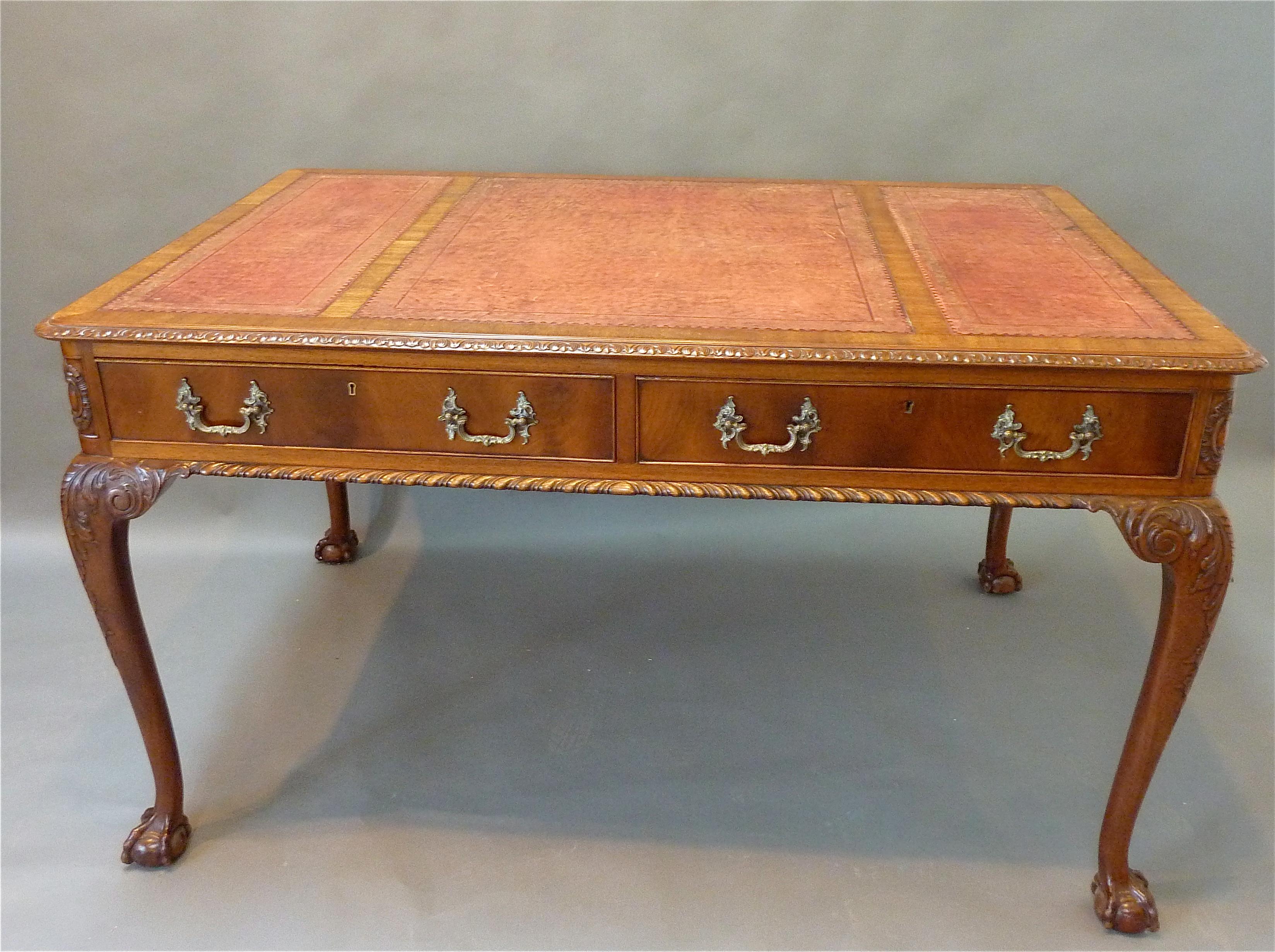 Made of Honduras mahogany with a rich faded patina. Original hand tooled and gilded red leather top with finely carved surrounding molding. Two “bookmatched” drawers retaining the original brass handles over boldly shaped cabriole legs with carved