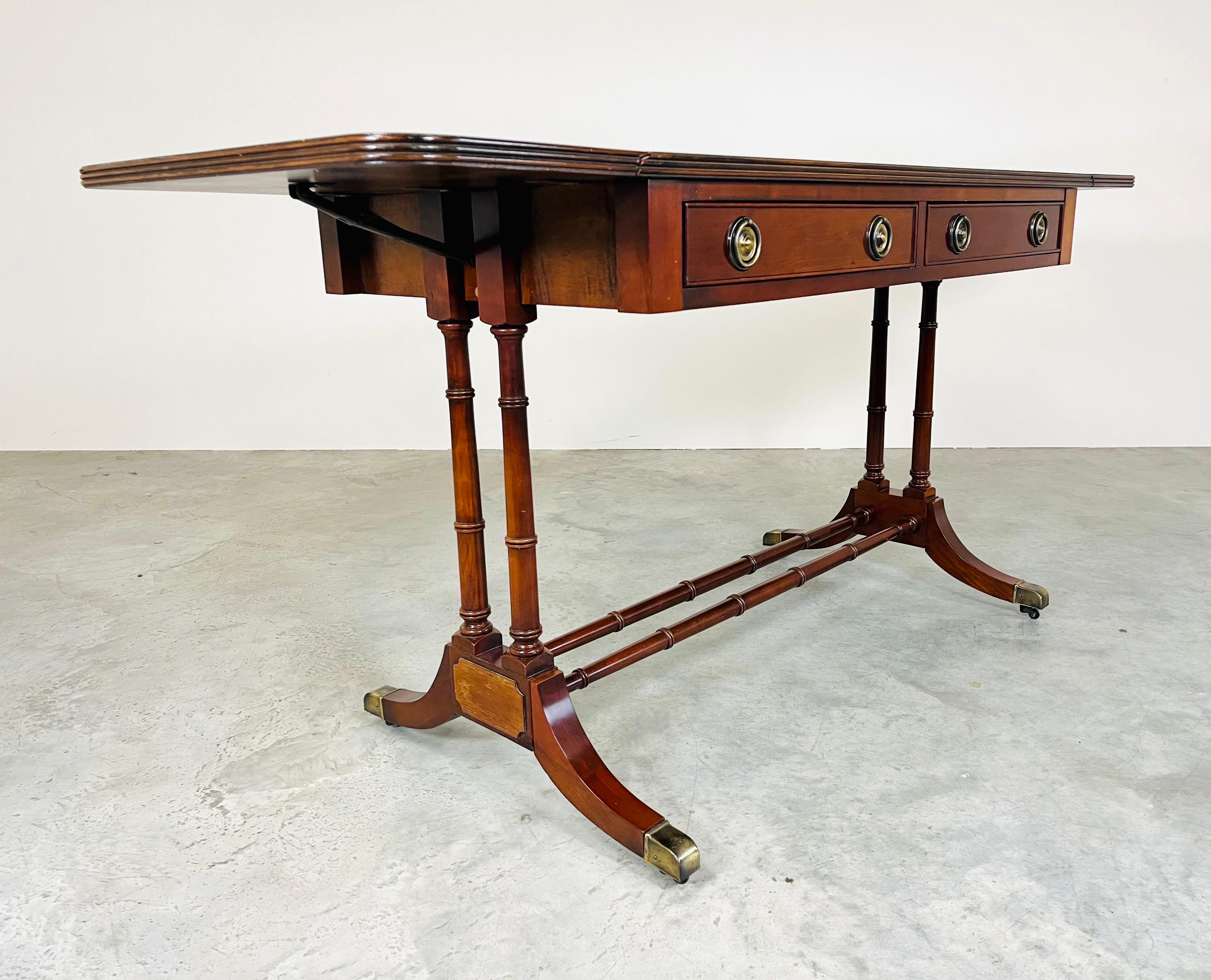 1930s Regency style drop leaf table. We love the unusual design & adjustable size having two dovetailed drawers, single turned faux bamboo stretcher having brass sabot feet over smooth brass casters. The original finish has been meticulously