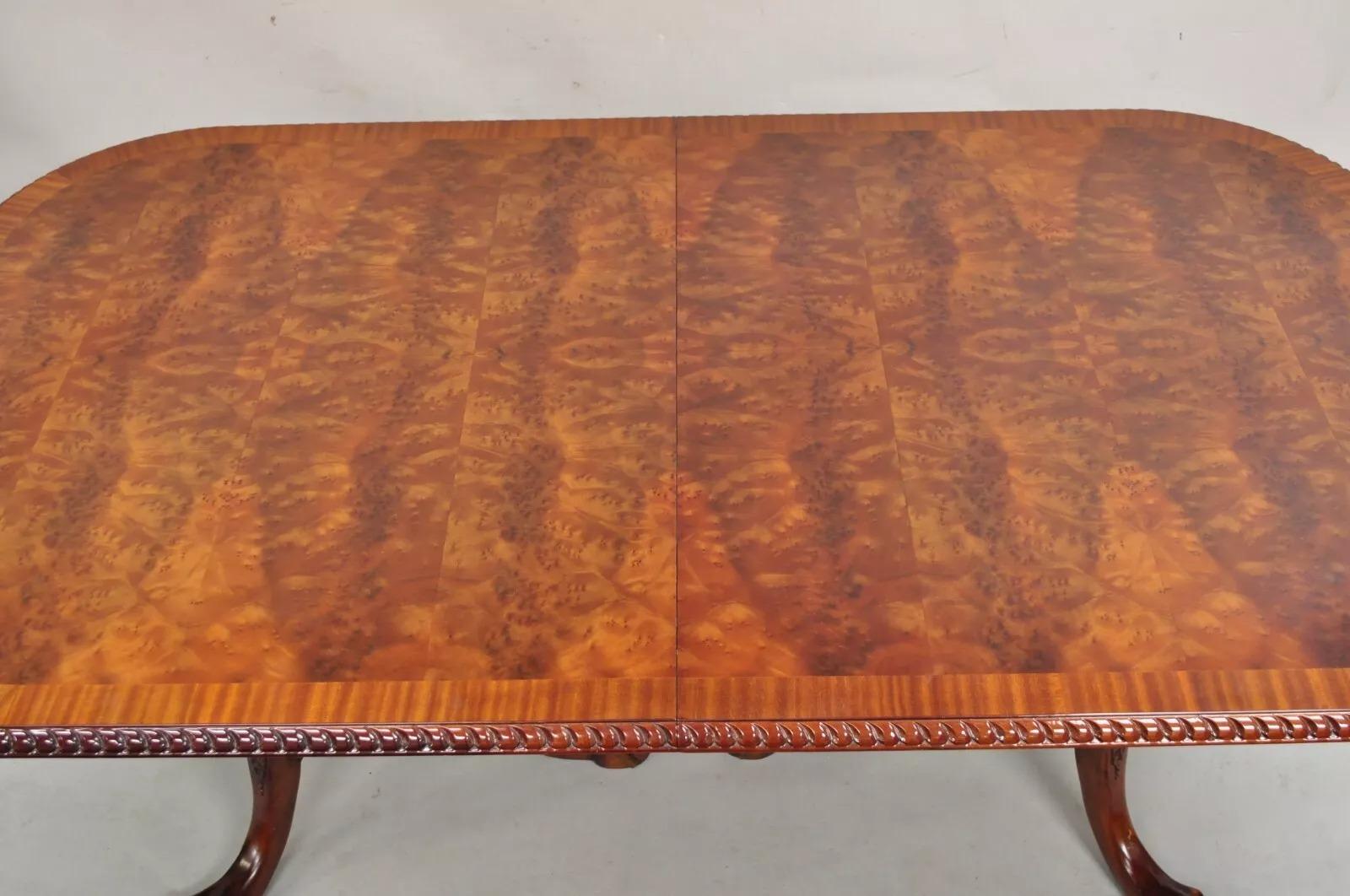 Reproducción de mesa de comedor de caoba flameada estilo Chippendale Ball and Claw con 2 hojas extensibles. El artículo presenta un borde tallado con cuerda, base de doble pedestal tallada con patas de bola y garra, impresionante tablero de caoba