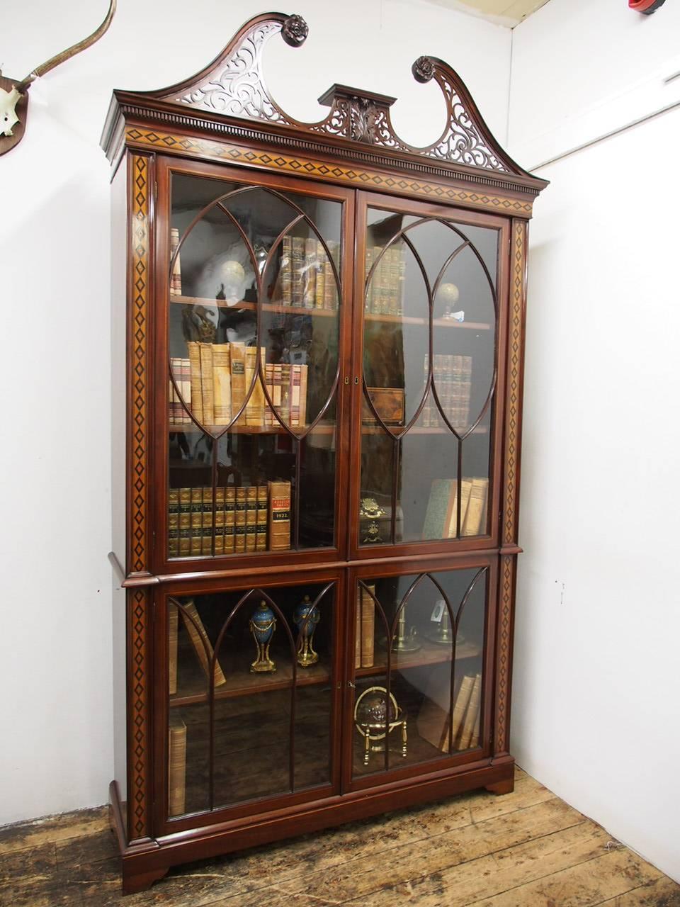 Chippendale style inlaid and glazed bookcase, circa 1870. With horn top pediment and carved roses to each end, it has open fretwork beneath it and a central platform decorated with carved acanthus leaves. It has a Greek dentil style cornice in