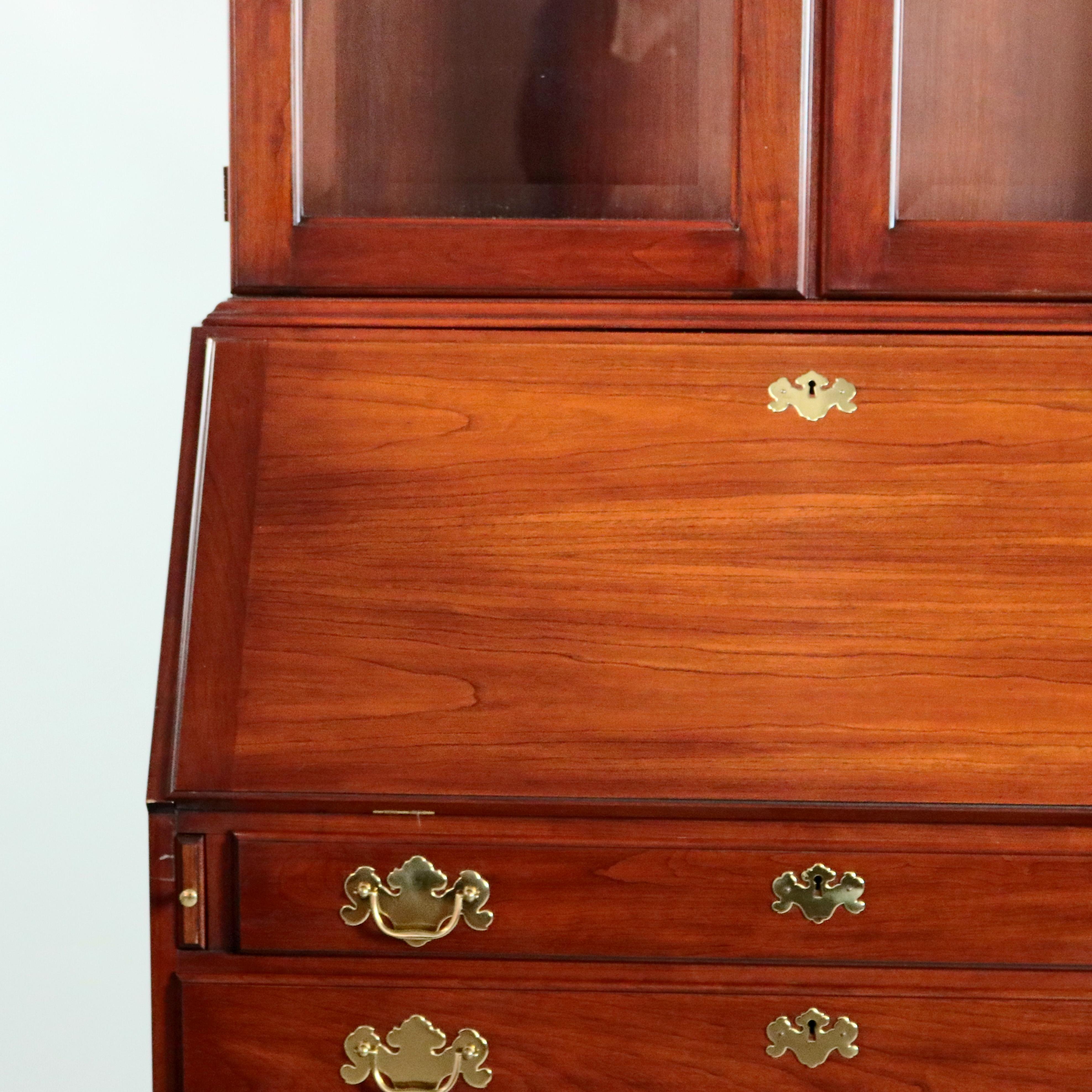 A Chippendale style secretary by Henkel Harris offers mahogany construction with double glass door bookcase opening to shelved interior and surmounting slant front desk with pull-out supports and interior storage compartments and pigeon holes, case