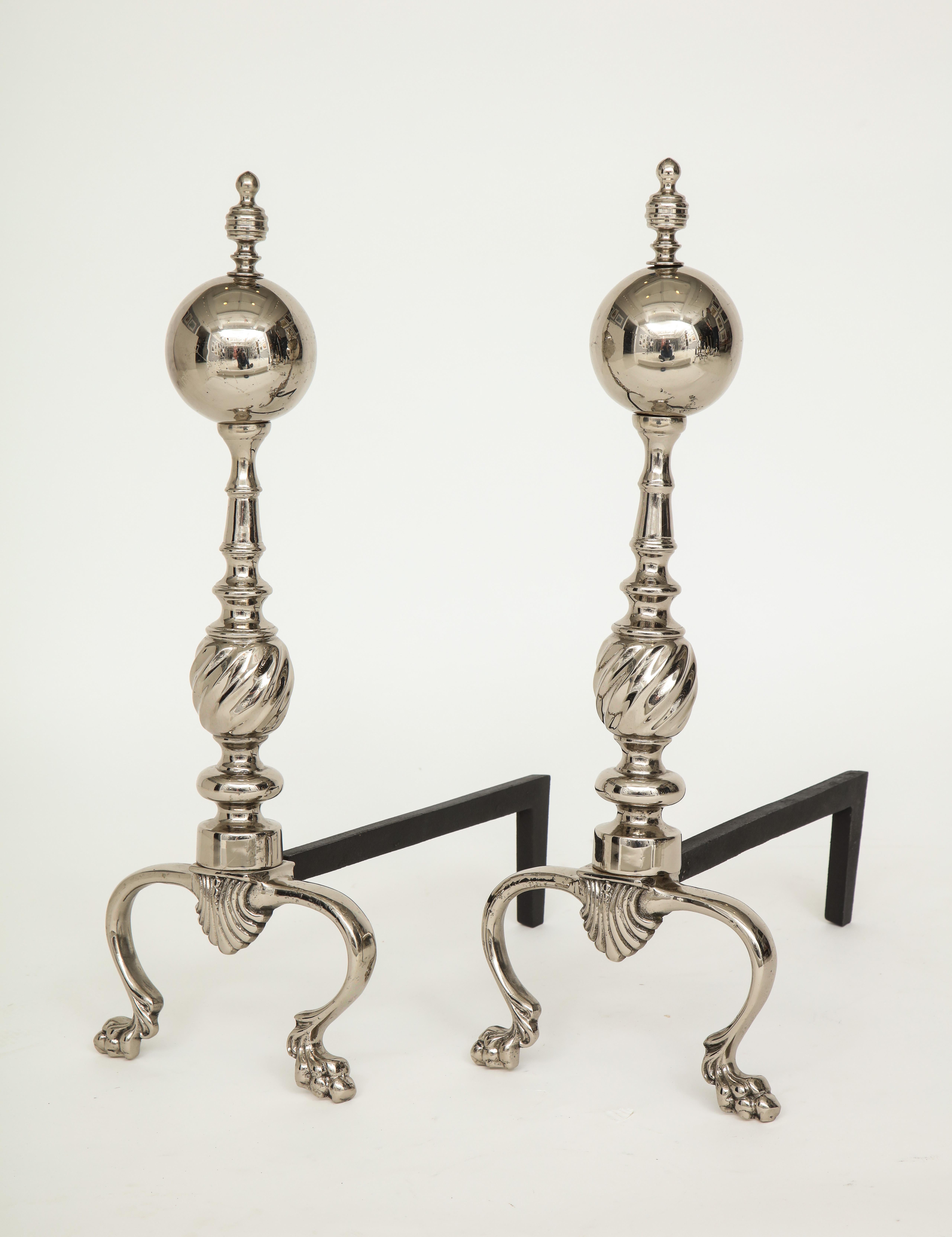 Pair of polished nickel andirons with cannonball finial, fluted body and stylized shell detail ending with claw/ball feet. New iron backs.