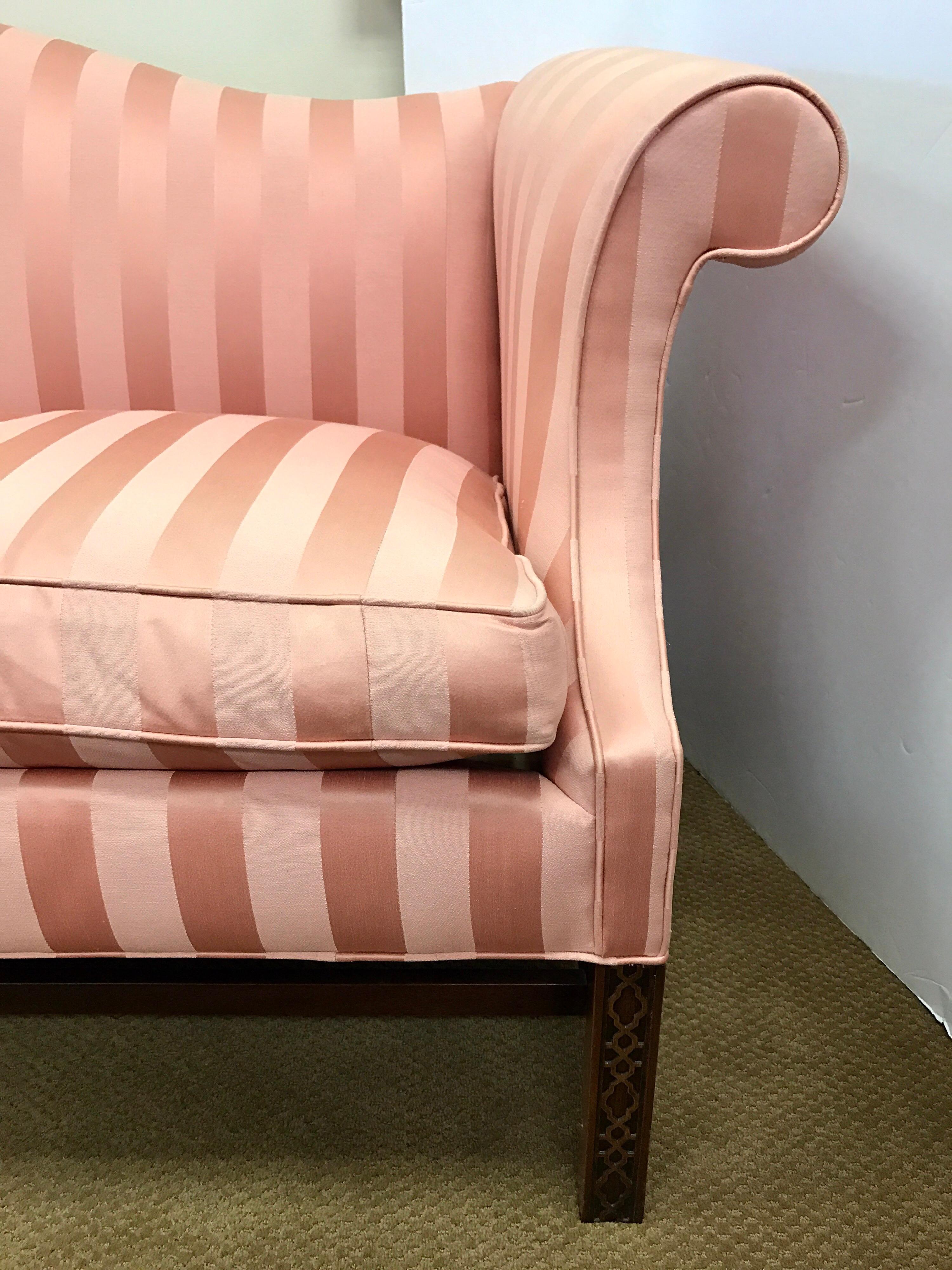 Classic Chippendale style camelback sofa with a mahogany frame with straight legs and stretchers, Chinese carved fretwork on front legs, upholstered in a pretty blush pink striped fabric with down/feather fill seat cushion.