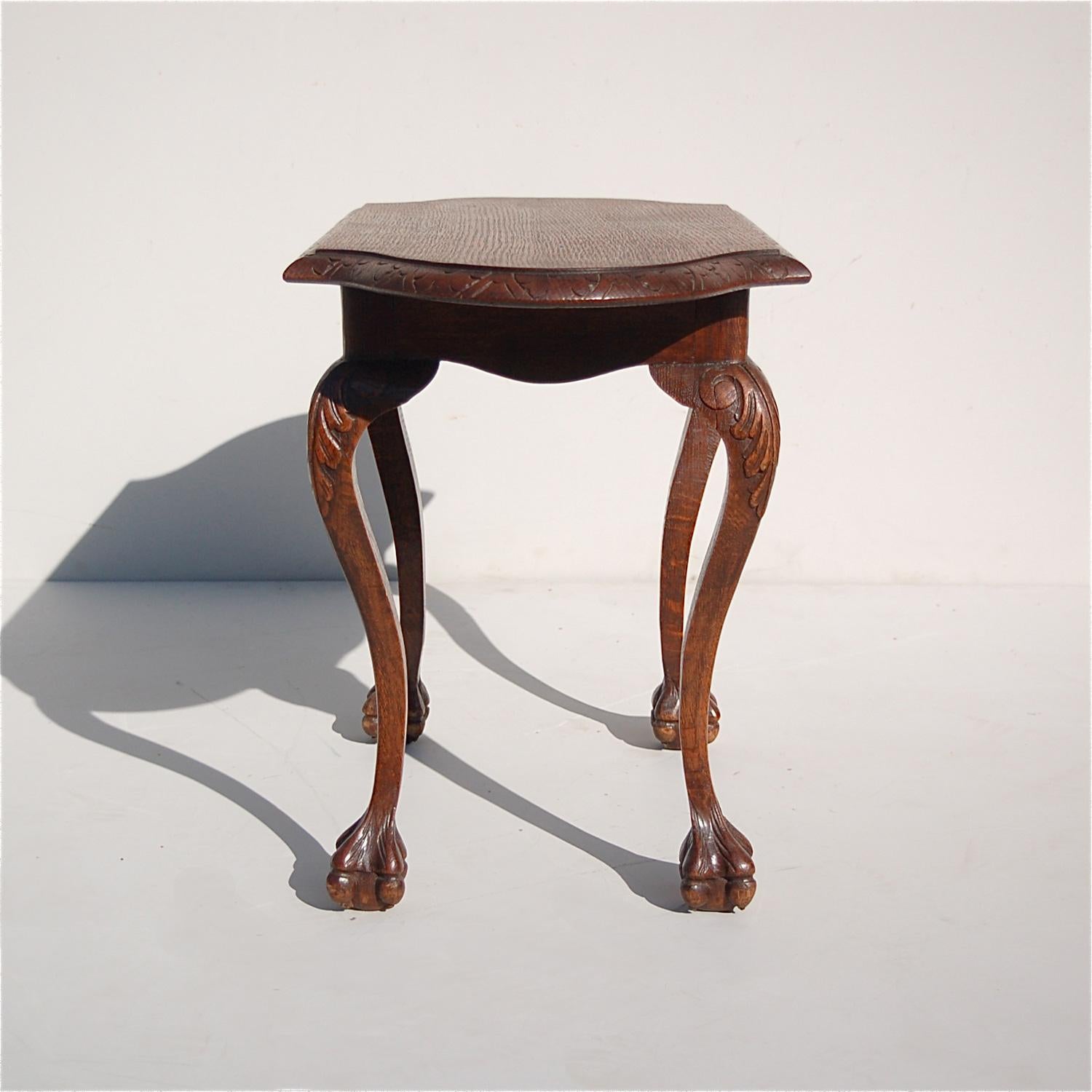 Delicately proportioned, low side table in the Chippendale style which combines usefulness with elegance. The table is made from solid oak. It has a rectangular top with scalloped or curved corners and lightly carved edging. The top is supported by