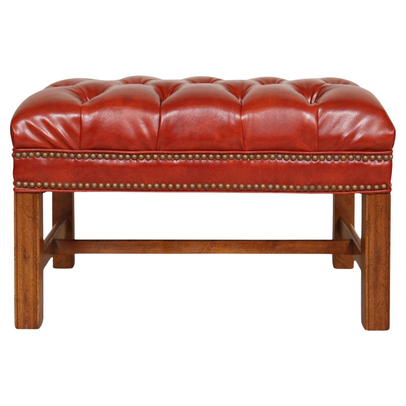 A Chippendale style tufted ottoman made by Sam Moore Furniture Industries. The diamond button tufted top is vinyl, with the look of leather, and four beveled legs are supported with an H-stretcher. Maker's label is visible underneath. 