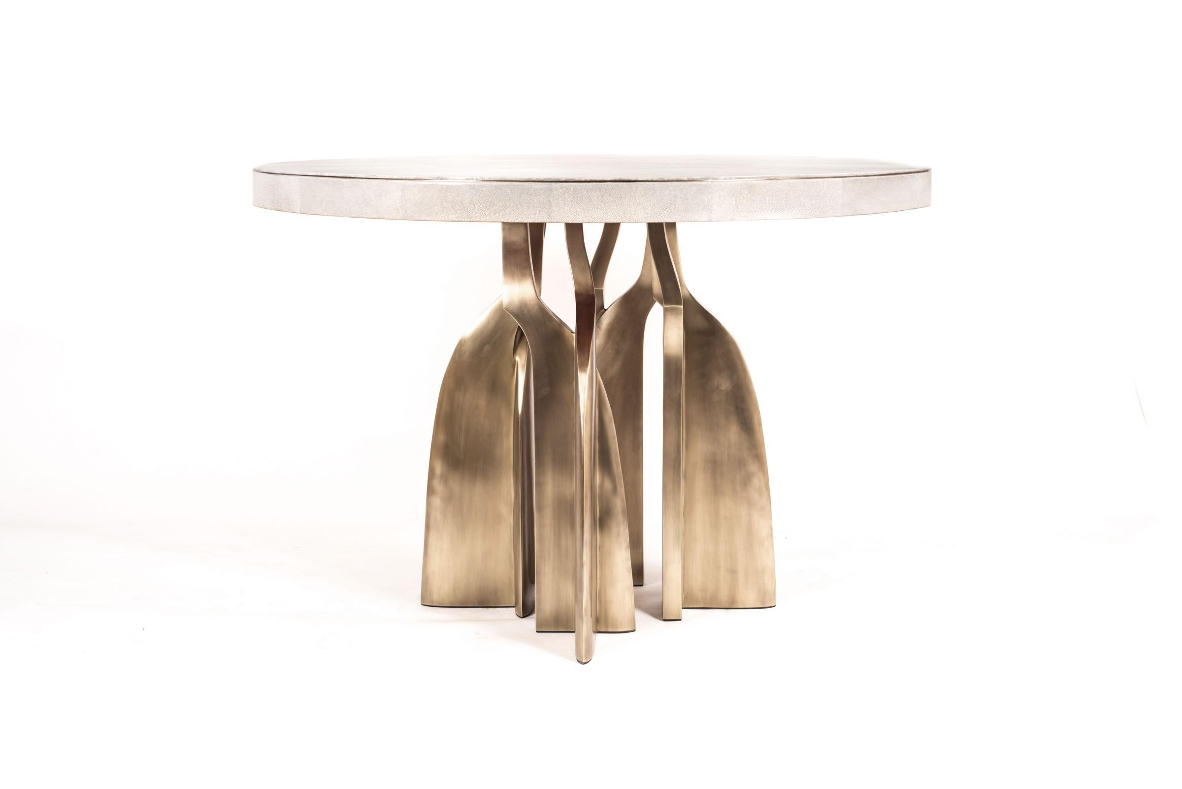 La table de petit-déjeuner Chital est une pièce étonnante, qui s'impose dans n'importe quel espace. Le plateau incrusté de galuchat crème présente un insert métallique subtil autour du cadre, suivi de pieds sculpturaux en laiton bronze-patiné