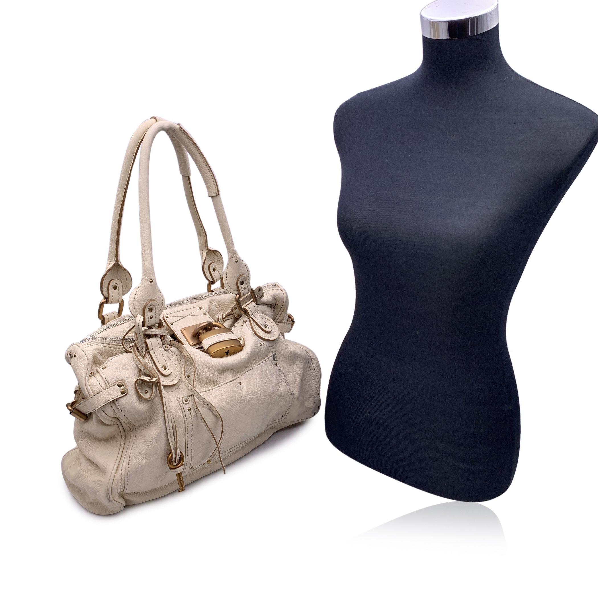 Gorgeous CHLOE 'Paddington Bag' crafted in genuine leather in a off white beige color. This bag features intense detailing such as chunky hardware, belting as well as two-rolled leather handles. At the top of the bag you will find the classic Chloe