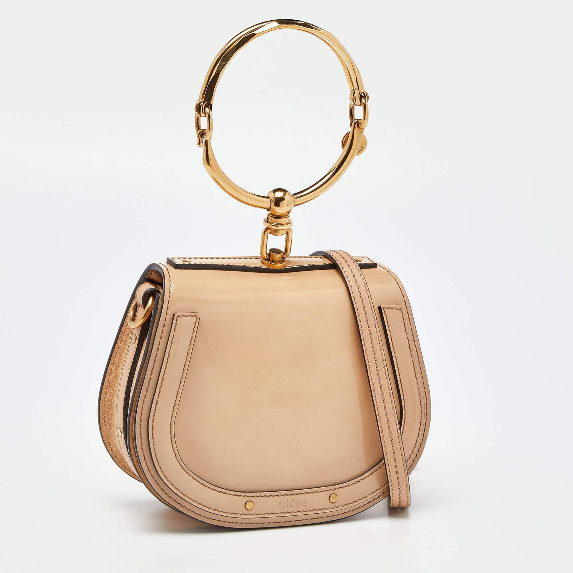 The Chloé Nile Bag is a luxurious and stylish accessory. Crafted from patent leather, it features intricate stud detailing and a unique bracelet handle. This compact crossbody bag exudes elegance and is perfect for carrying essentials while making a