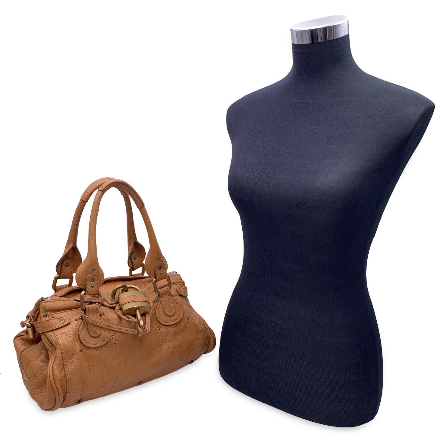 Gorgeous CHLOE Paddington Bag' crafted in genuine leather in a tan beige color. This bag features intense detailing such as chunky hardware, belting as well as two-rolled leather handles. At the front of the bag you will find the classic Chloe