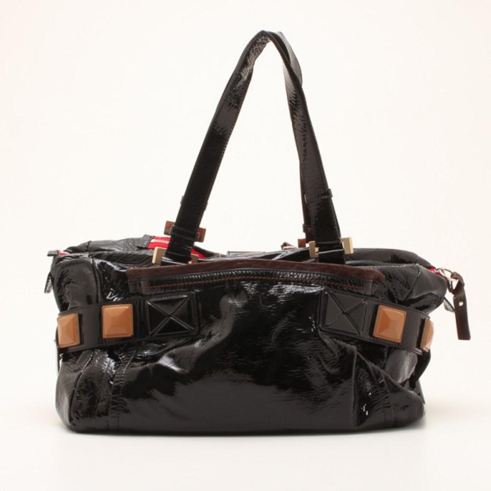 This Chloe handbag in patent black lambskin leather is a must have. It features red leather trim and front and back patch pockets. The strap bears leather pyramid detailing that complements the patent pyramid feet at the bottom. The interior is