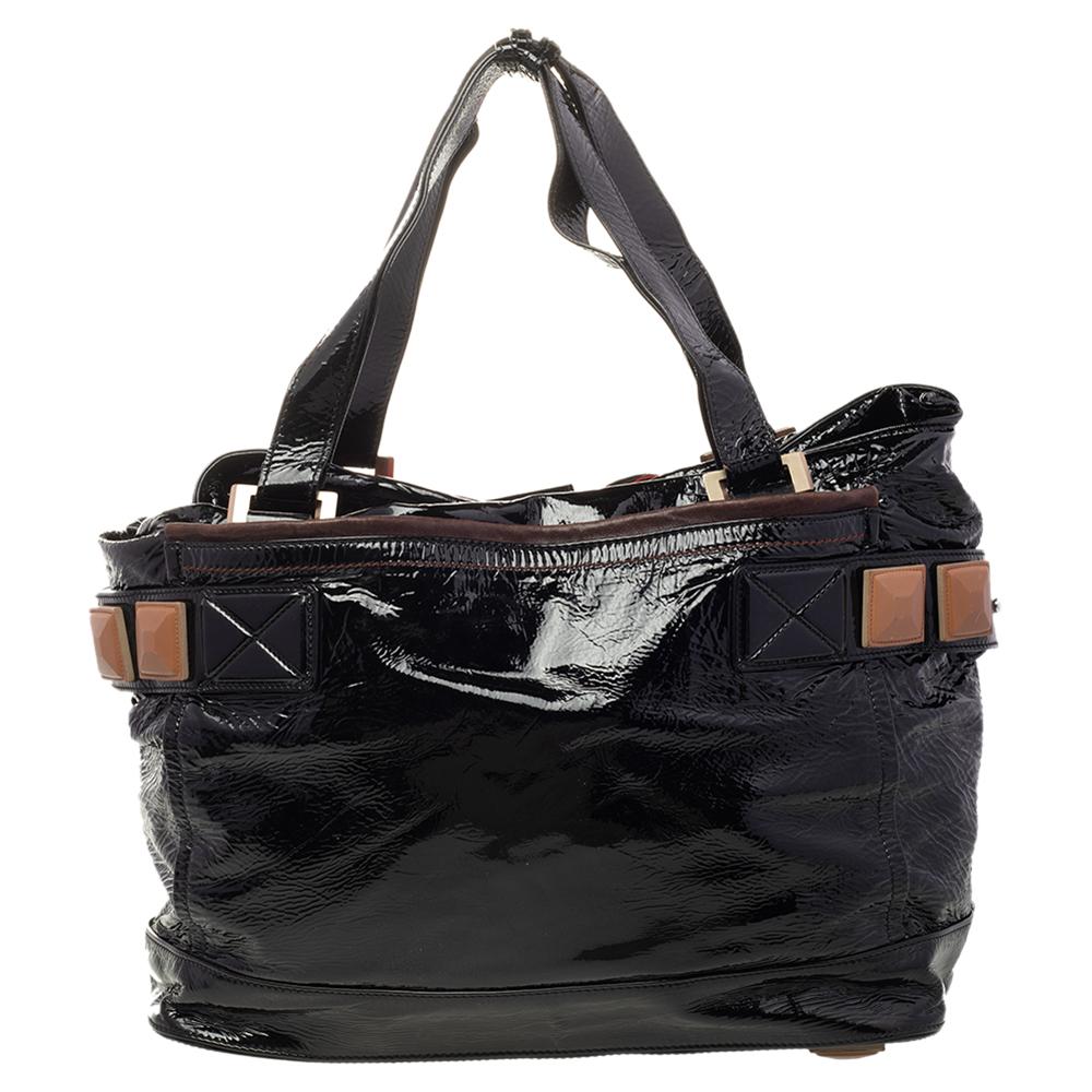 This Chloe tote in black patent leather is a must-have. It features contrasting leather trims and front & back open compartments. The strap bears leather pyramid detailing that is in tune with the pyramid feet at the bottom. The interior is lined