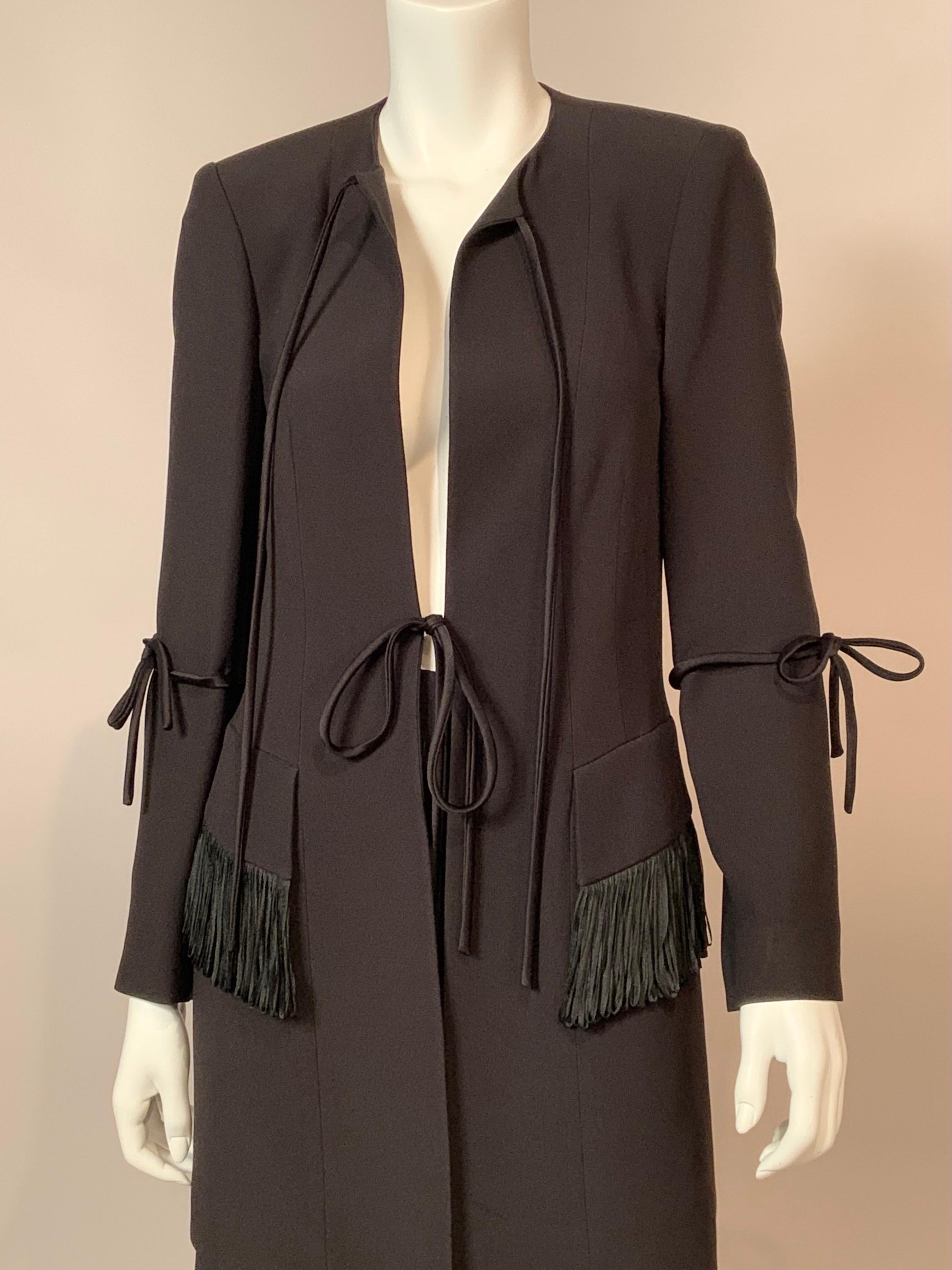 Karl Lagerfeld designed this stunning black silk evening suit with a long jacket and skirt.  The jacket has two long black satin ties for closure, one at the neckline and one at the waist. There is looped satin fringe on both pocket flaps, and the