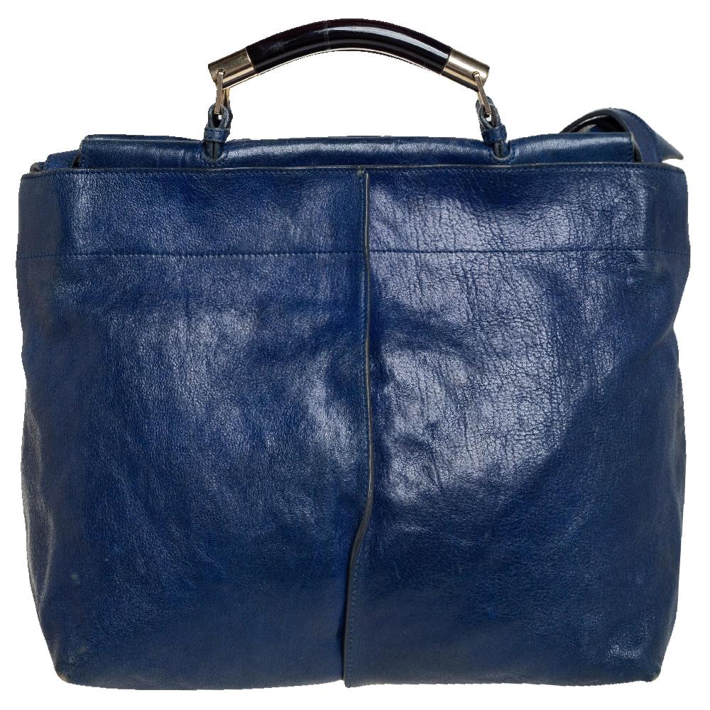The Saskia satchel by Chloé is a briefcase-style bag that one can carry for work or travel. It is made of blue leather and complemented by gold-tone hardware. The bag has a top handle, a shoulder strap, front pockets, and a canvas interior.
