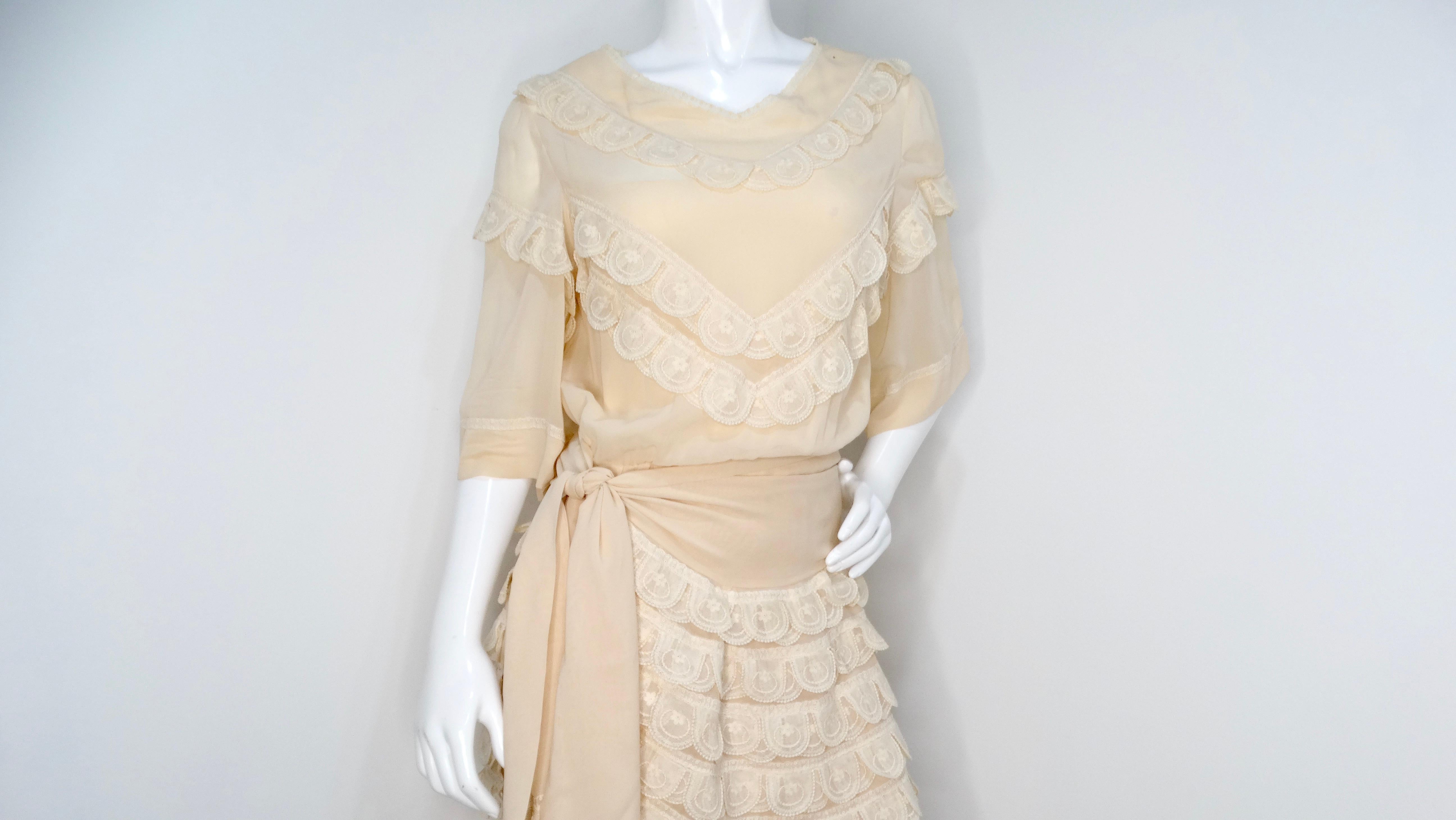 The Chloe by Karl Lagerfeld Circa 1970s Cream Blush Tiered Lace & Pleated Dress is a timeless testament to romantic elegance. This exquisite piece features a soft cream blush hue with an enchanting silhouette that cinches at the waist, highlighting