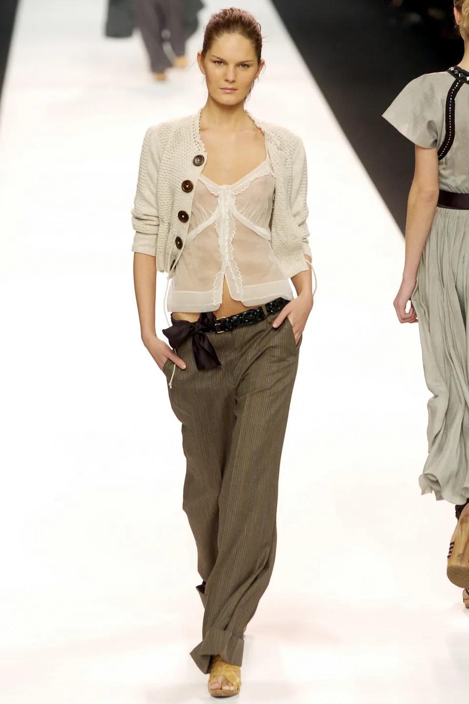 Chloé by Phoebe Philo Strickjacke aus cremefarbener Merinowolle, Herbst Winter 2004
Erschien auf dem Laufsteg sowie an Daria Werbowy in der amerikanischen Vogue im August 2004
Überdimensionale Holzknöpfe
Beschnittene Silhouette
Krawatten-Detail in