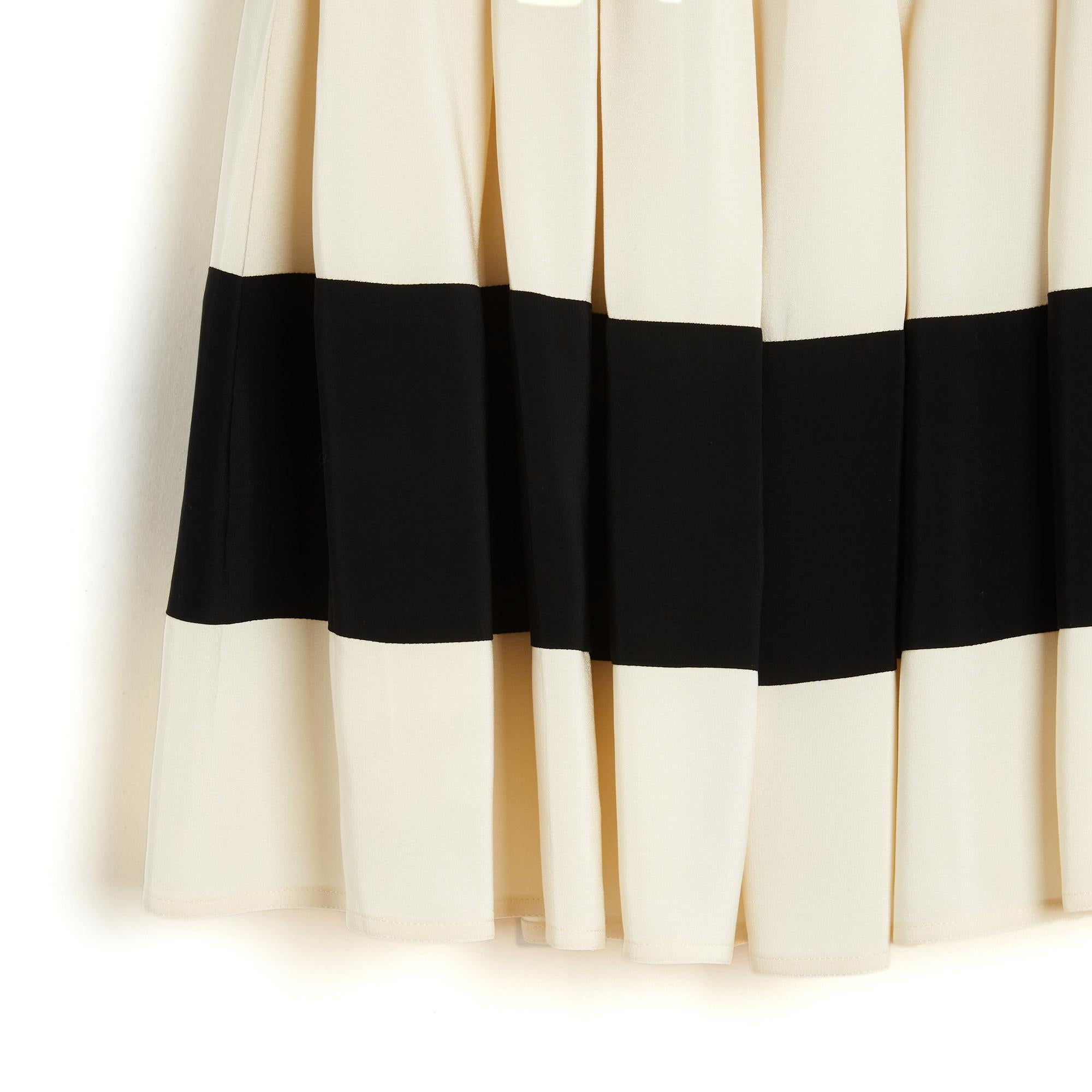 Chloé skirt circa 1990 in thick ecru silk crepe decorated with a wide black band, box pleats stitched on the hips (flat) to the top of the thighs, closing with a zip and 3 hooks, lining in matching satin canvas edged with ecru lace. Size indicated