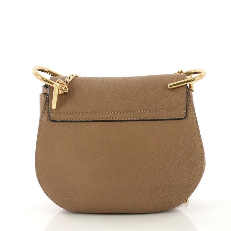 This Chloe Drew Crossbody Bag Leather Small, crafted in beige leather, features a long chain strap accented with oversized U-shaped rings and gold-tone hardware. Its oversized turn-lock closure opens to a beige suede interior with slip pocket.
