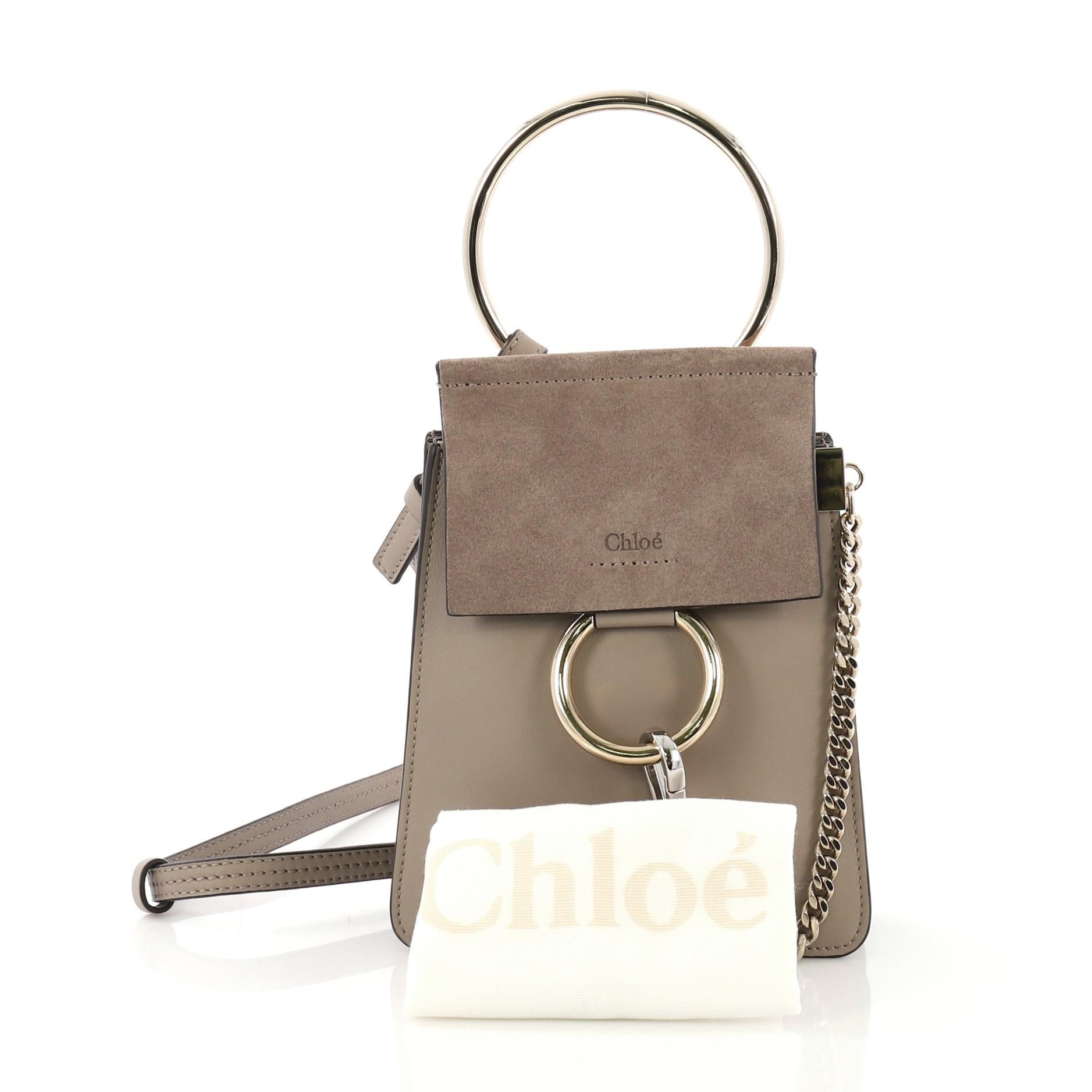 This Chloe Faye Bracelet Crossbody Bag Leather and Suede Mini, crafted from taupe leather, features an adjustable crossbody strap, ring detail and chain, side snap buttons, and gold-tone hardware. Its magnetic snap closure opens to a taupe suede