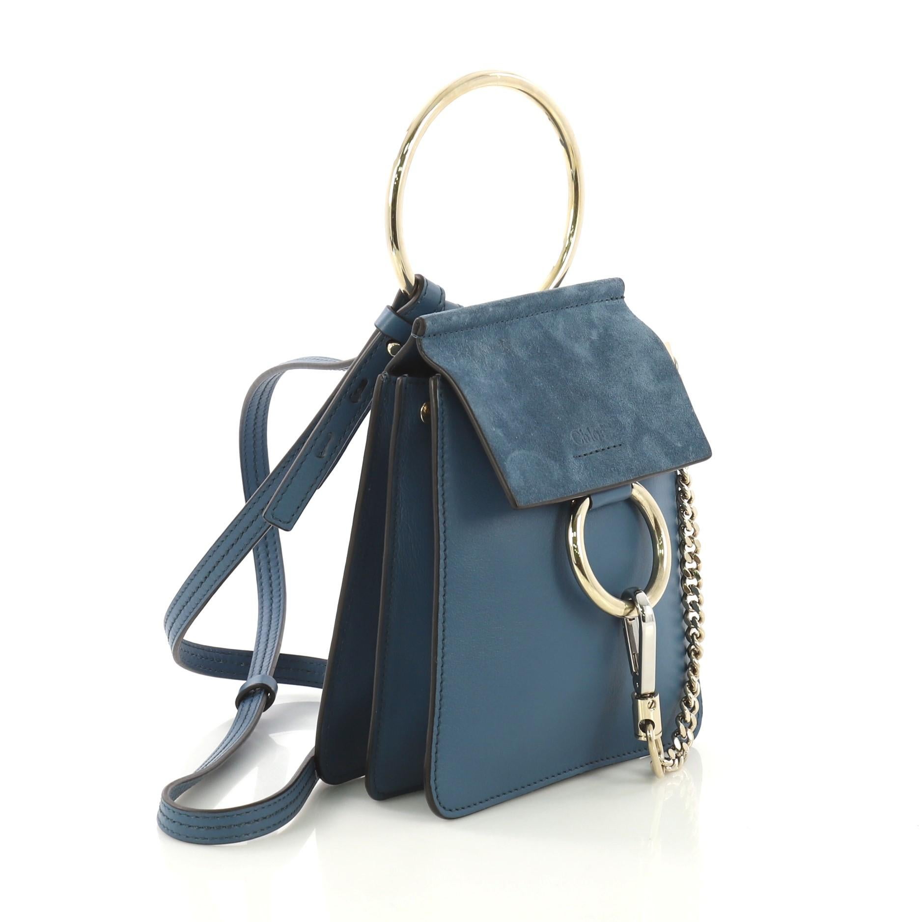 This Chloe Faye Bracelet Crossbody Bag Leather and Suede Mini, crafted from blue leather, features an adjustable crossbody strap, ring detail and chain, side snap buttons, and gold and silver-tone hardware. Its magnetic snap closure opens to a beige