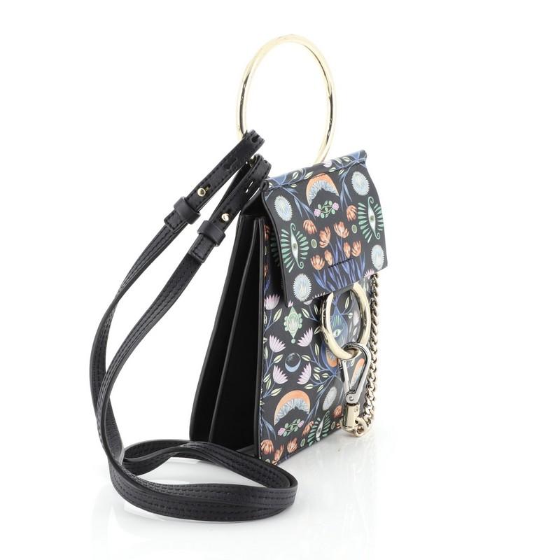 This Chloe Faye Bracelet Crossbody Bag Printed Leather Mini, crafted from black printed leather, features detachable, adjustable crossbody strap, ring detail and signature chain, side snap buttons and gold and silver-tone hardware. Its magnetic snap
