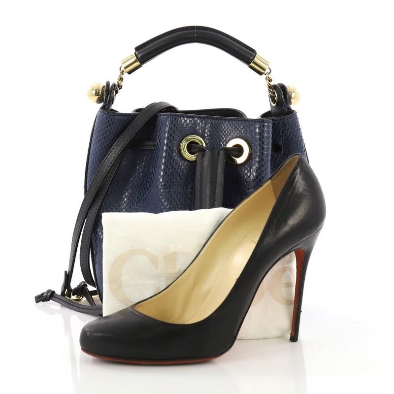 This Chloe Gala Bucket Bag Python Small, crafted from genuine blue python, features a rolled top handle with chain insets and gold-tone hardware. Its drawstring closure opens to a beige fabric interior. **Note: Shoe photographed is used as a sizing