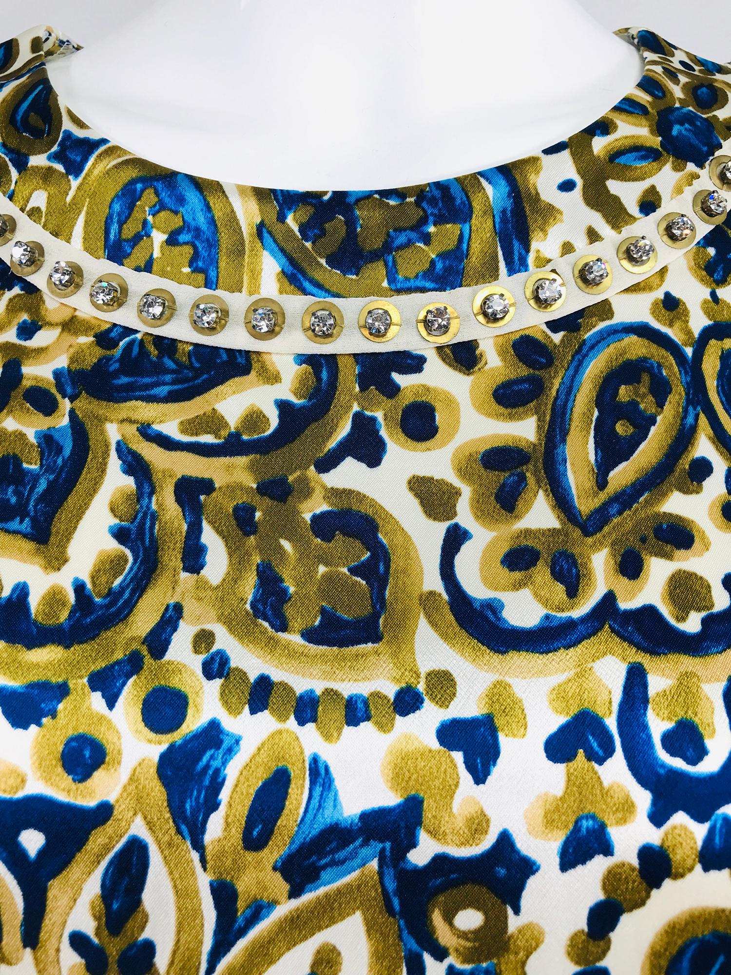 Chloe' gold and blue rhinestone jewel neckline blouse. Abstract print on a cream ground in blue and gold, the round neckline has a circular band of crystal rhinestones. 3/4 length sleeves have cuff vents. The blouse is hip length pull on style it