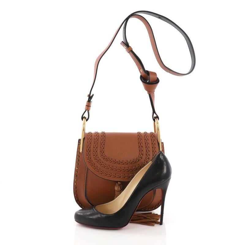 This Chloe Hudson Handbag Whipstitch Leather Small, crafted from brown leather, features an adjustable long flat shoulder strap with signature knot, whipstitched trims, front suede tassel, and gold-tone hardware. Its flap opens to a beige suede
