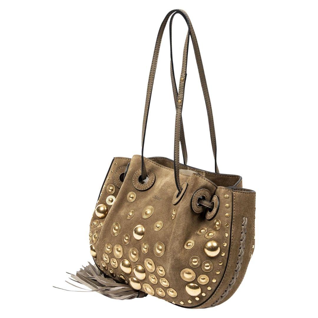 The light brown suede leather exterior is studded for a chic look, and it closes with a gold drawstring. Inside, the canvas lining includes one slip pocket.

SPECIFICS
Length: 10.3
Width: 1.8
Height: 7.9
Strap drop: 10
Authenticity code: