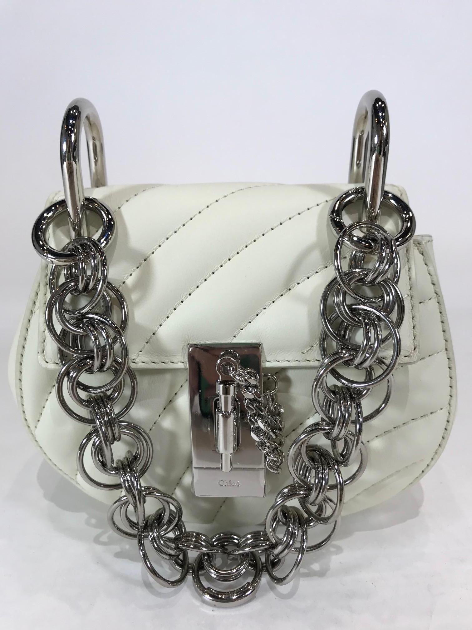 White Quilted Leather. Silver-tone hardware. Pin and clasp-fastening at front flap closure. Features bracelet-inspired chain-link handle, Beige suede interior with slip pocket. Estimated Retail Price: $1,590