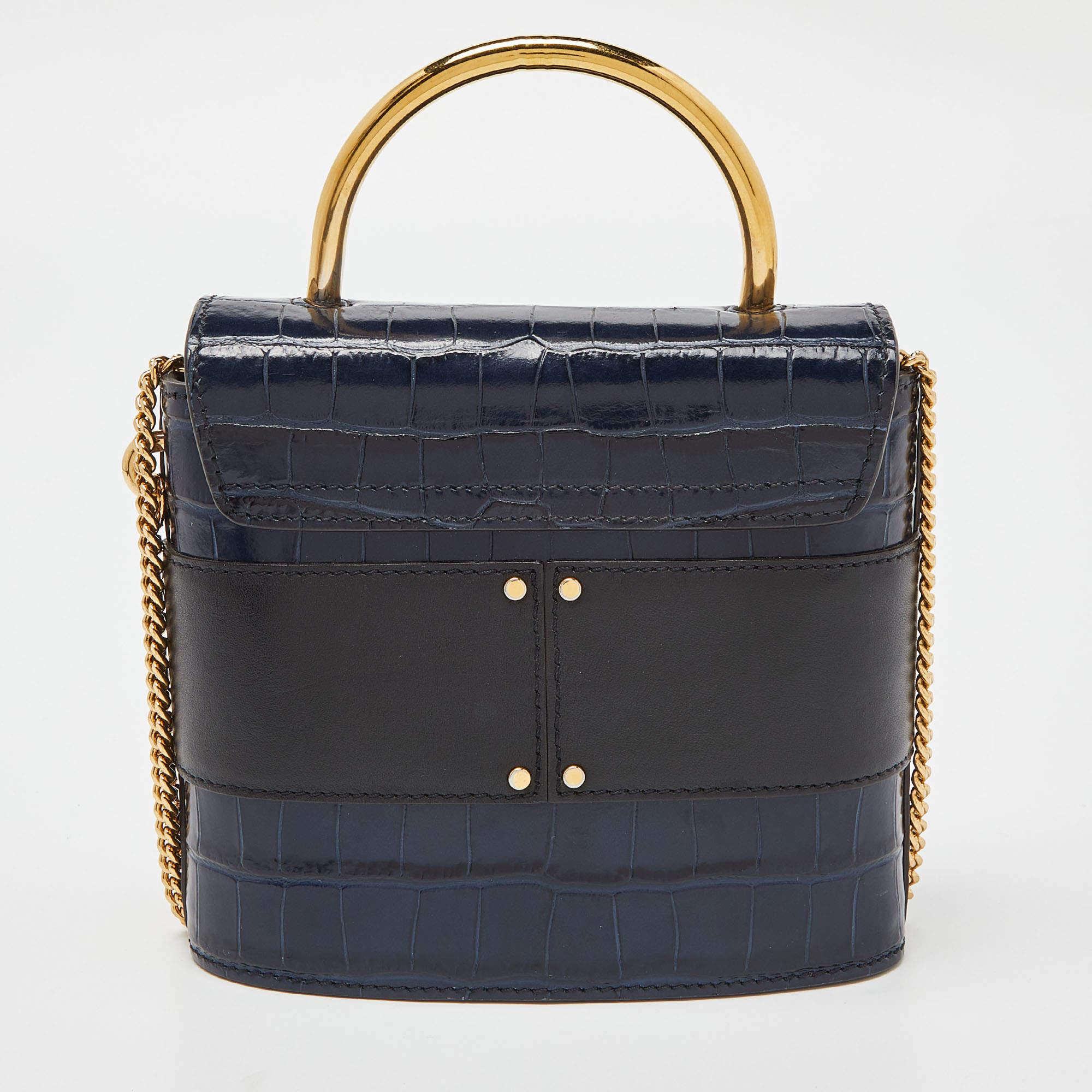 With an affinity to create chic bags that look like works of art, Chloe brings this Aby Lock bag that is just a masterpiece. Crafted from croc-embossed leather, it presents itself in a blue and black hue. It is styled with a front flap that carries