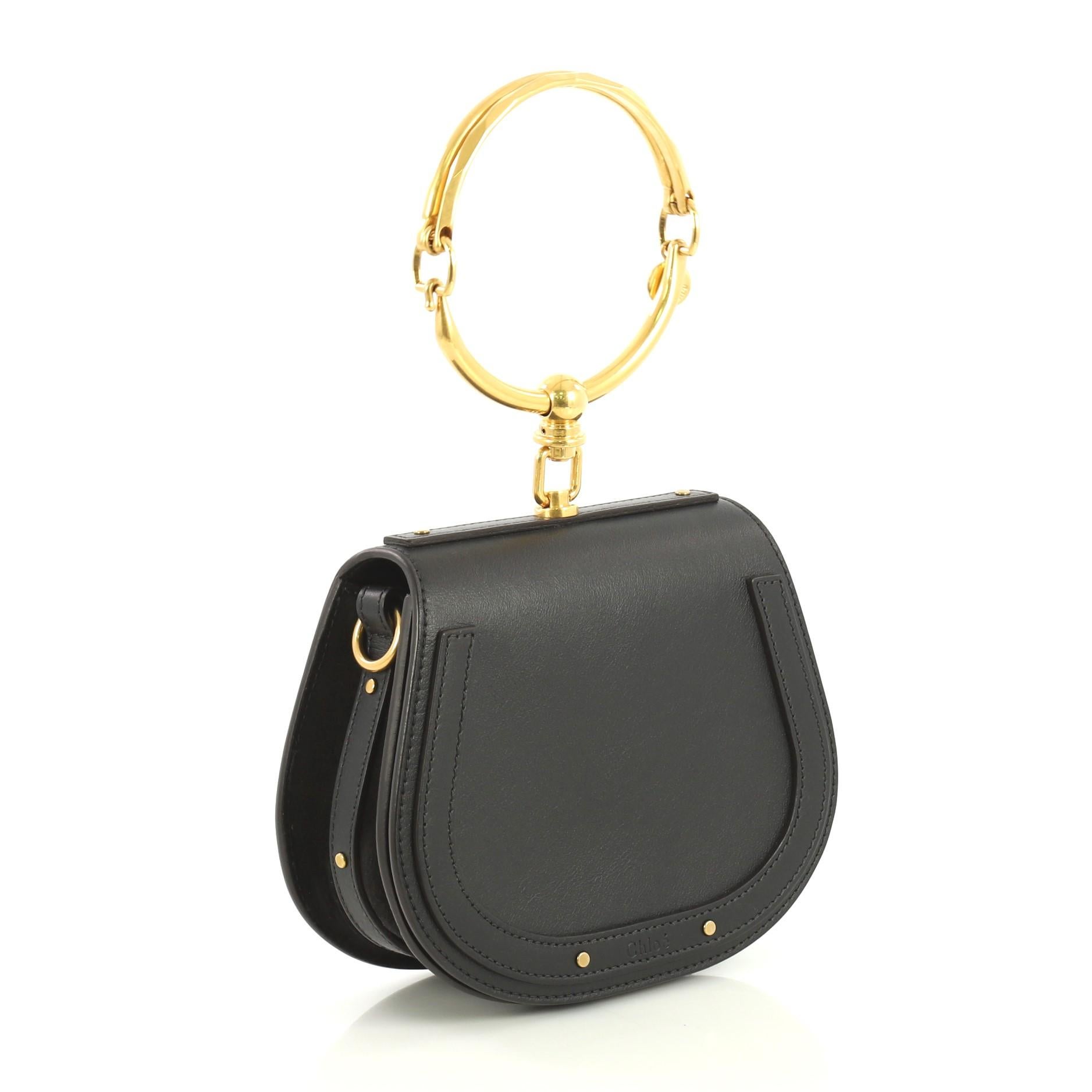 This Chloe Nile Crossbody Bag Leather Small, crafted from black leather, features ring bracelet handle, exterior back slip pocket, and aged gold-tone hardware. Its magnetic snap button closure opens to a neutral suede interior with slip pocket.
