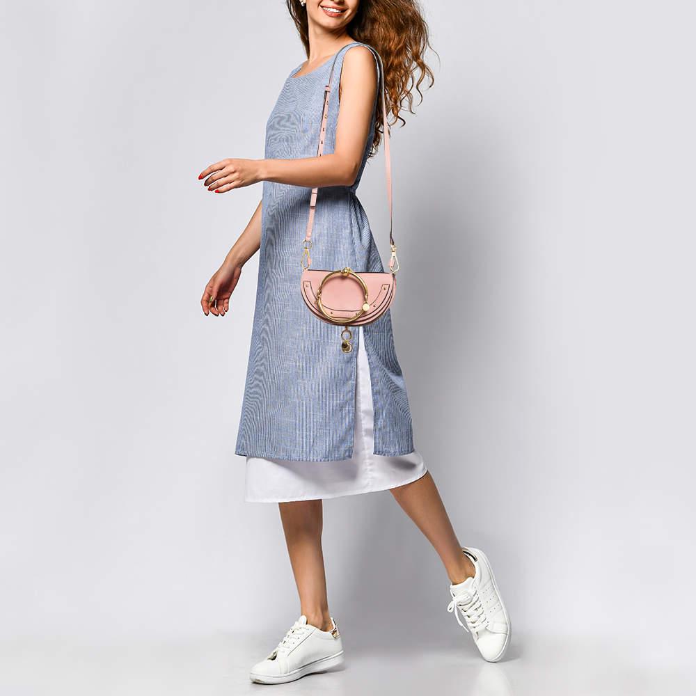 This Nile bag by Chloe can become your most favorite bag thanks to its unique shape and bracelet handle. This crossbody bag has been crafted using pink leather and styled with a front flap that opens to a leather lined interior. It is complete with