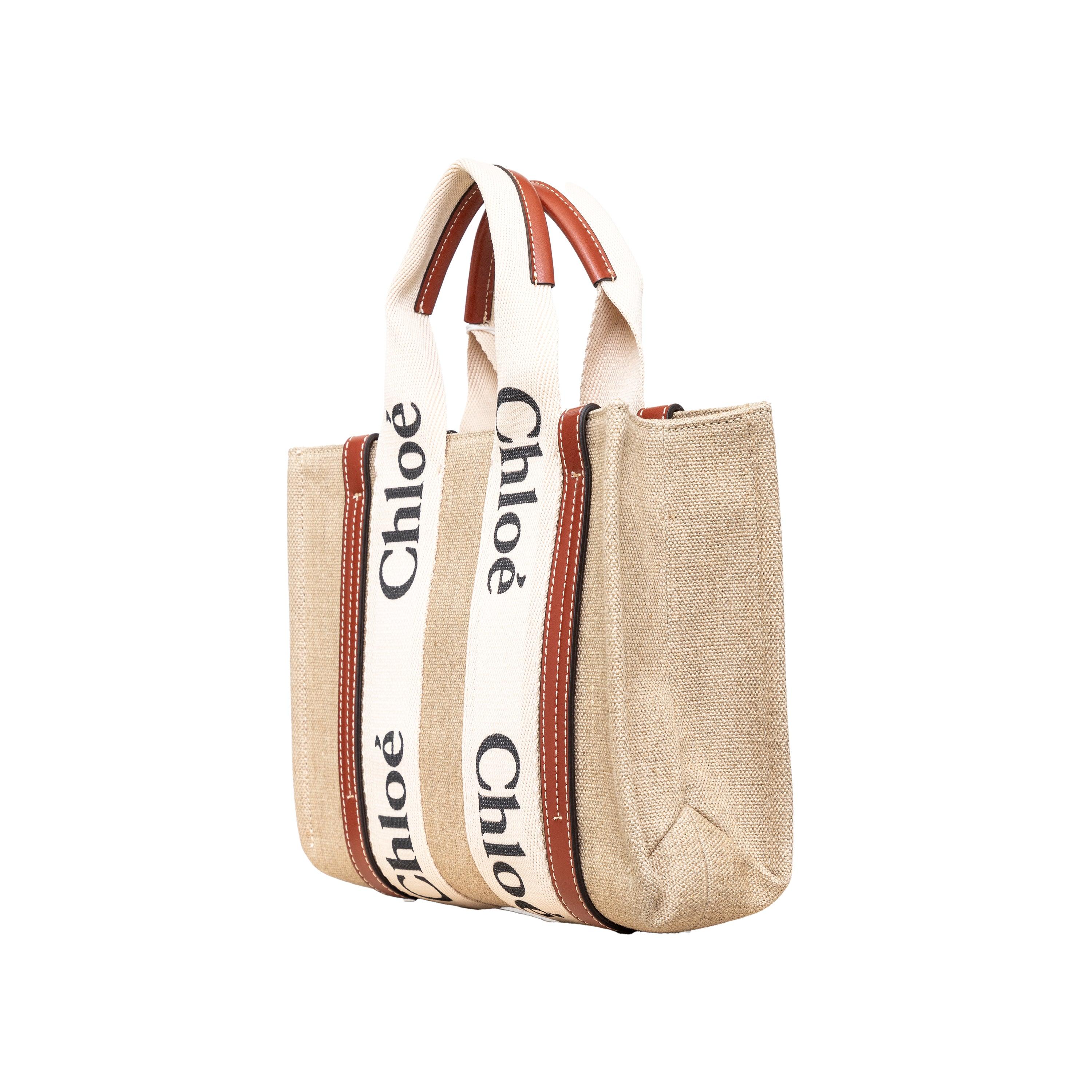 Effortlessly chic and environmentally conscious, the small Chloé Woody Tote Bag is crafted from lower-impact linen canvas and shiny brown calfskin strips. This compact bag features a roomy unlined interior with a practical leather shoulder strap and