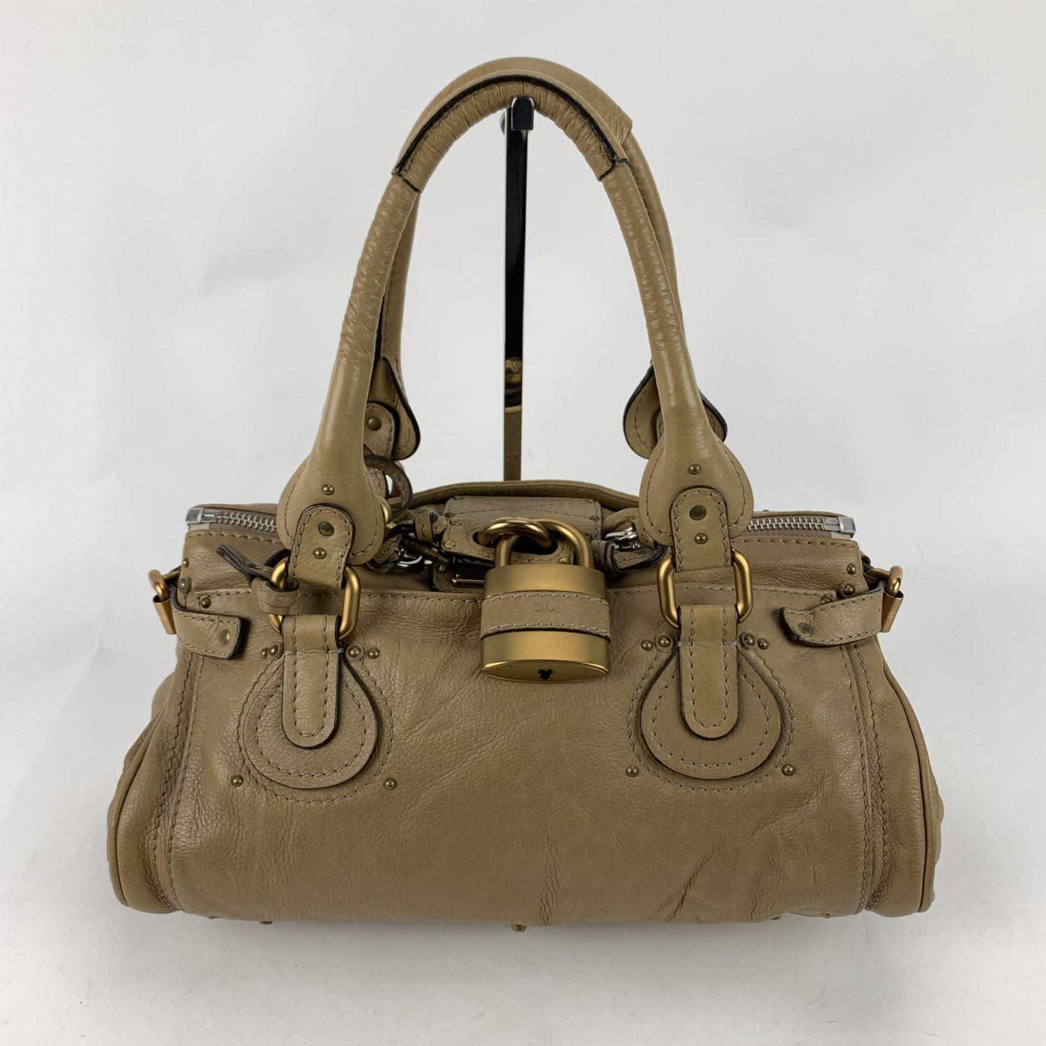 Gorgeous CHLOE 'Paddington Bag' crafted in genuine leather in a tan beige color. This bag features intense detailing such as chunky hardware, contrasted stitching and belting as well as two-rolled leather handles. At the front of the bag you will